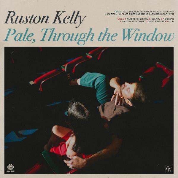 Albumcover: Ruston Kelly, „Pale, Through the Window“. Zwei Personen umarmen sich im gedämpften Licht, umgeben von roten Stühlen.