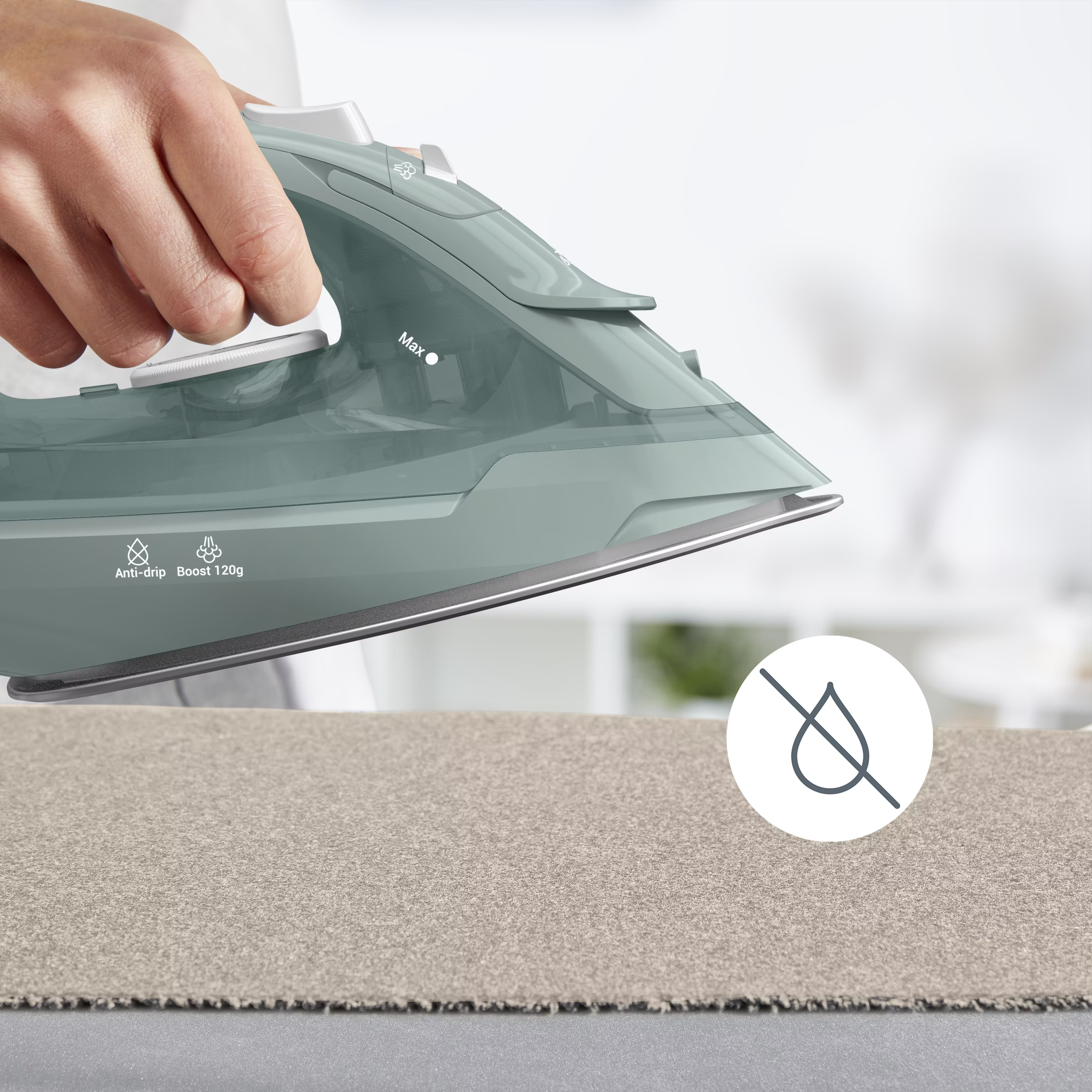 Une personne repasse un tissu beige avec un fer vert. Le fer a une fonction anti-goutte et un symbole anti-goutte.