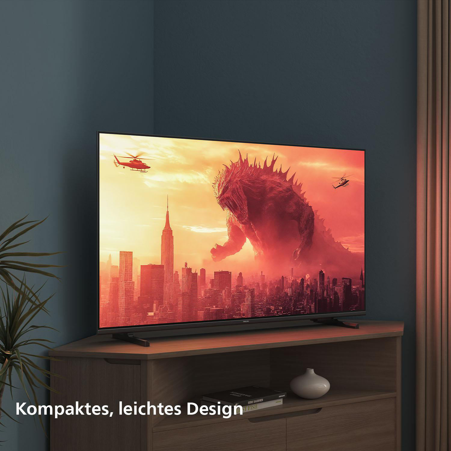 Der Fernseher zeigt ein rotes Monster über einer Stadt. Hubschrauber fliegen. Der Fernseher steht auf einem Holzschrank.