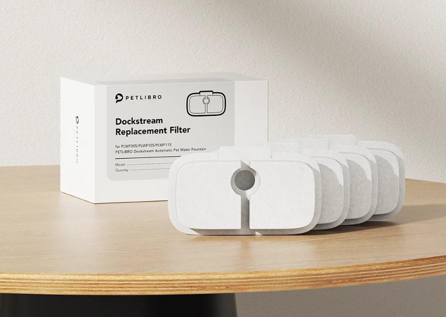 Eine PETLIBRO Dockstream Ersatzfilterbox und mehrere Filter stehen auf einem Holztisch vor einer weißen Wand.