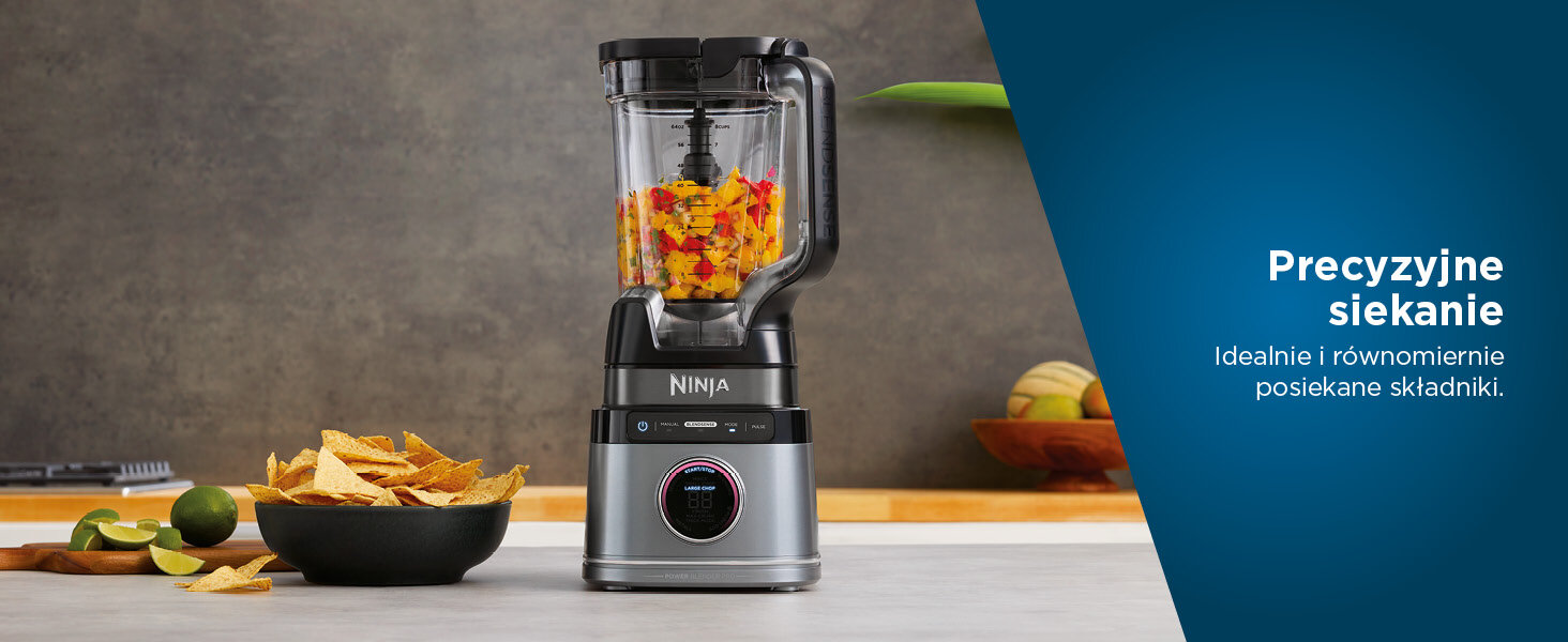 Blender Ninja z posiekanymi warzywami w środku. Na stole chipsy tortilla i limonki. Niebieskie tło po prawej.