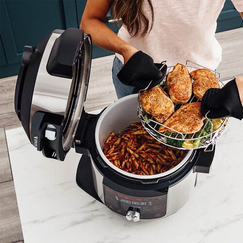 Osoba wyjmuje ugotowanego kurczaka z szybkowaru z makaronem. Szybkowar jest otwarty. Używane są rękawice.