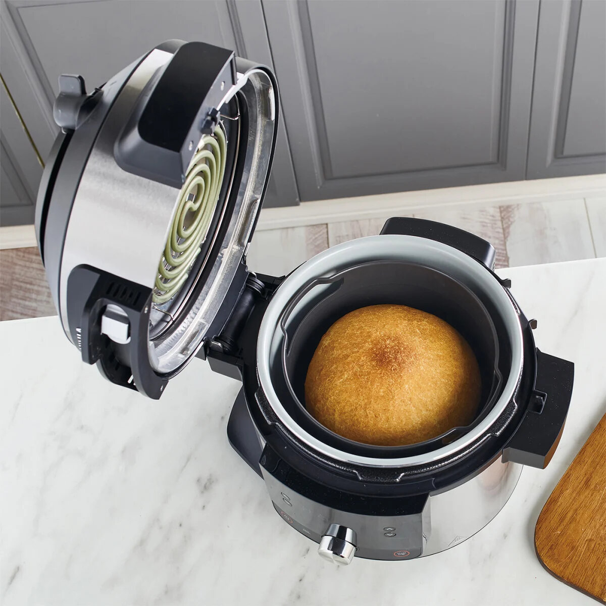 Otwarta frytkownica powietrzna z chlebem w środku. Tło przedstawia blat i szafkę.