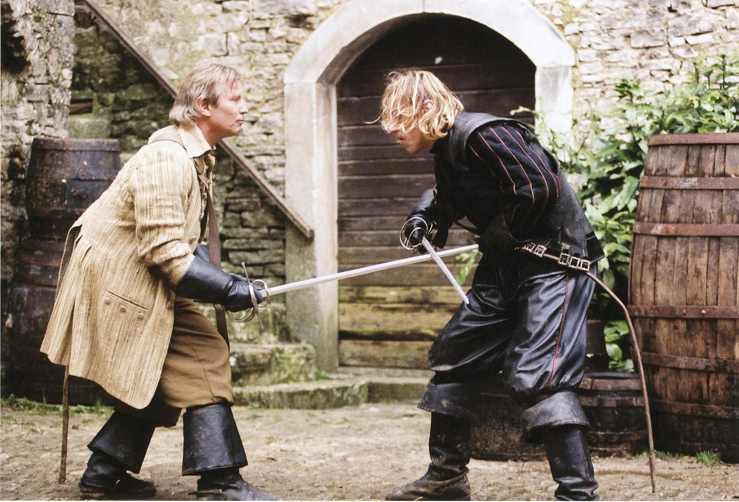 Zwei Männer in historischer Kleidung duellieren sich mit Schwertern. Einer trägt Beige, der andere Schwarz, in einem Innenhof mit Fässern.
