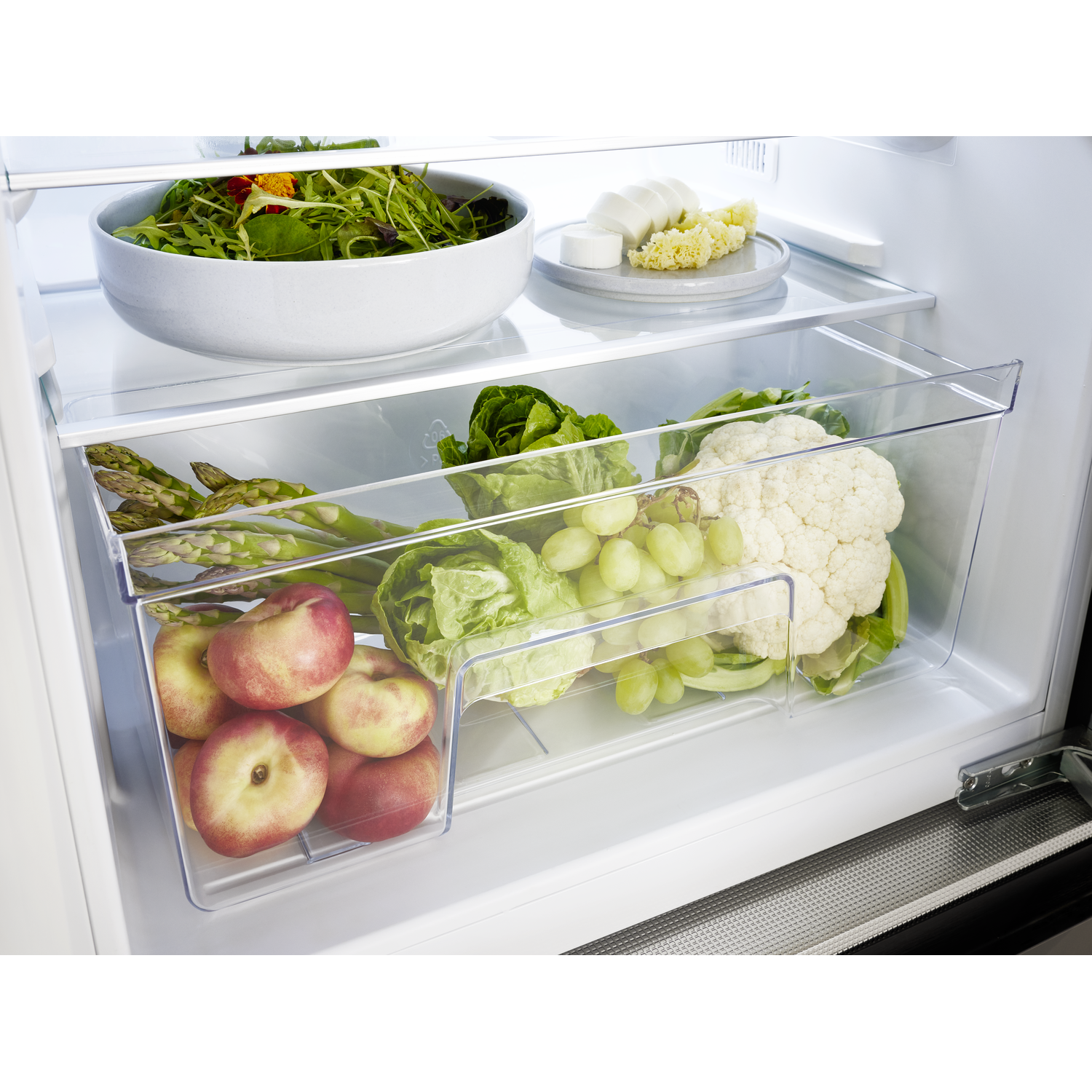 Refrigerator interior with fruits and vegetables. Peaches, asparagus, cauliflower, grapes, lettuce, and salad are visible.