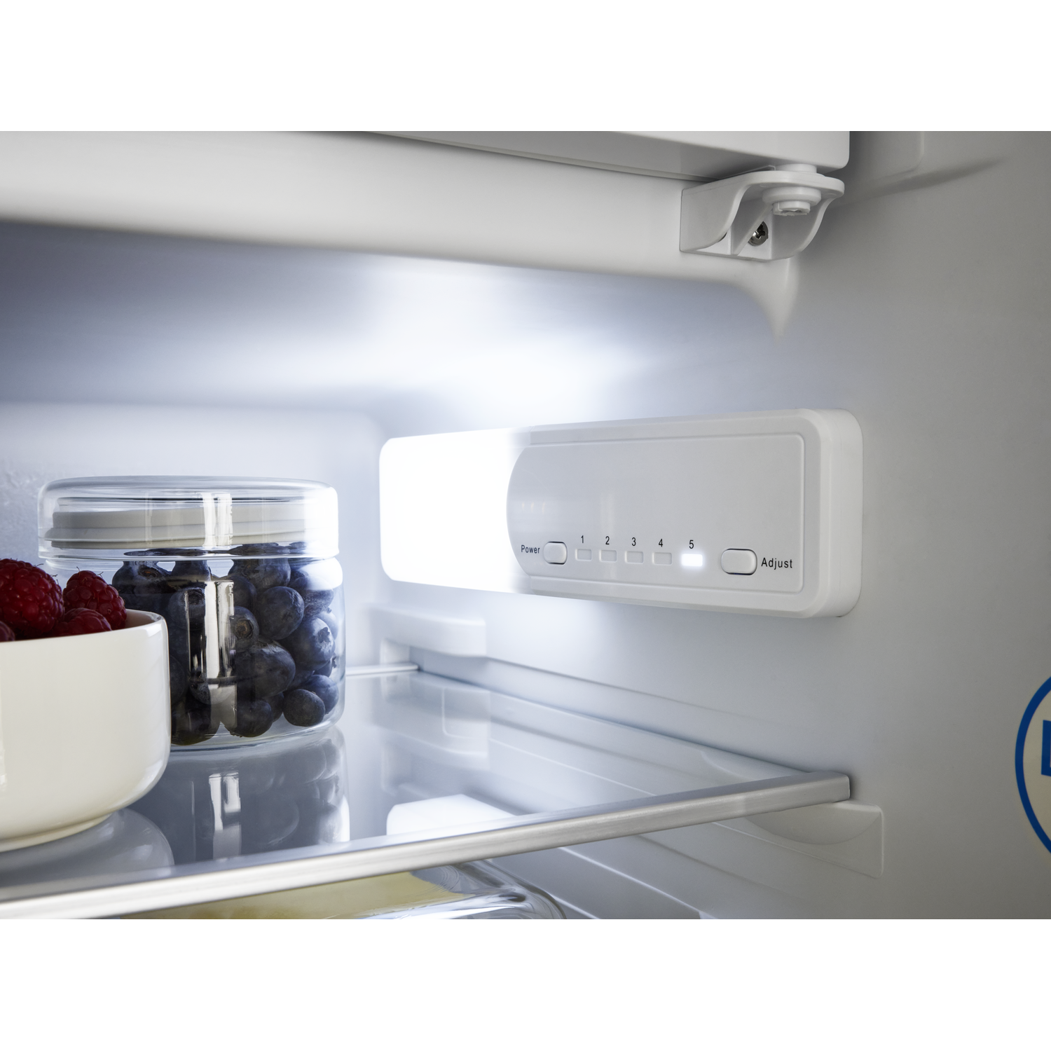 Inside a refrigerator, white control panel with lights, berries in a jar and bowl.