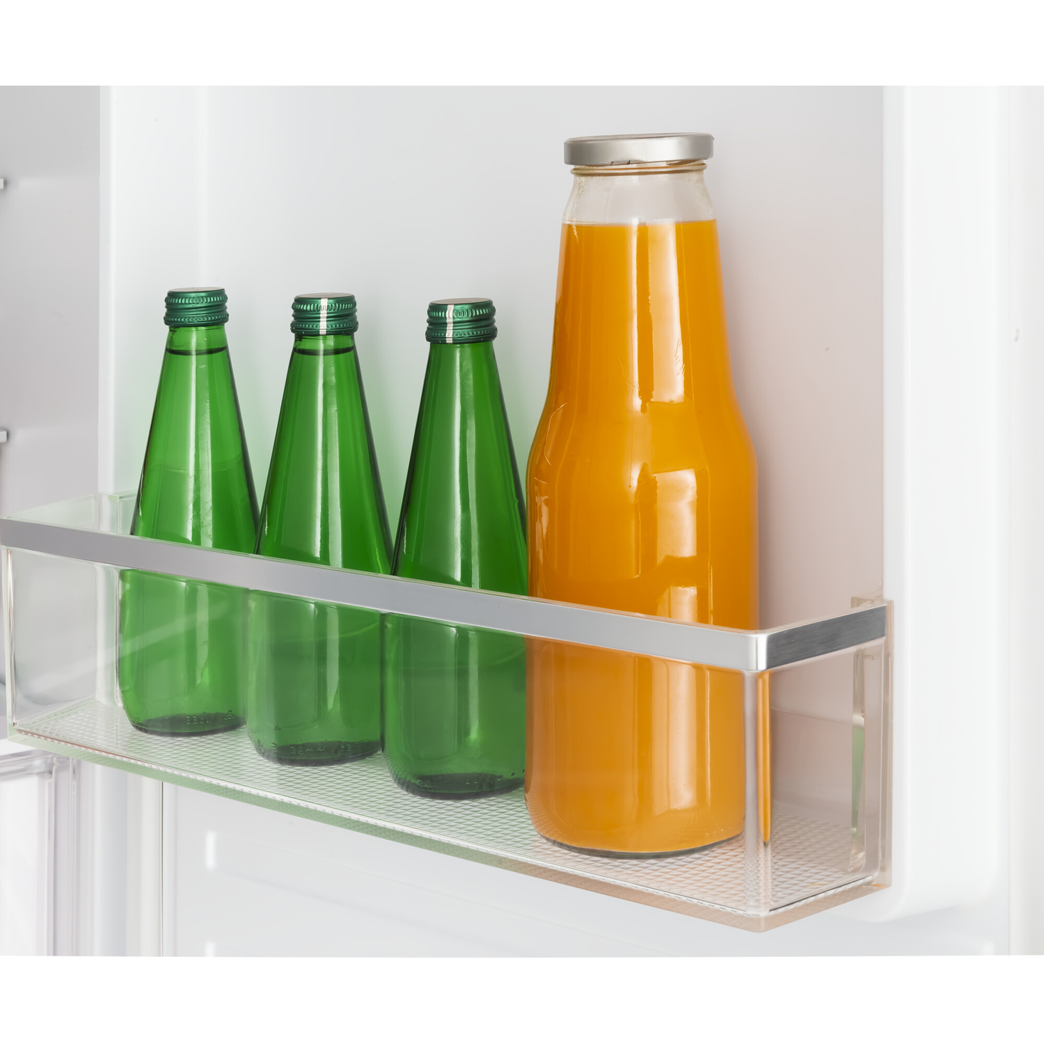 Inside a fridge, there are three green glass bottles and one orange juice bottle. The bottles are on a shelf.