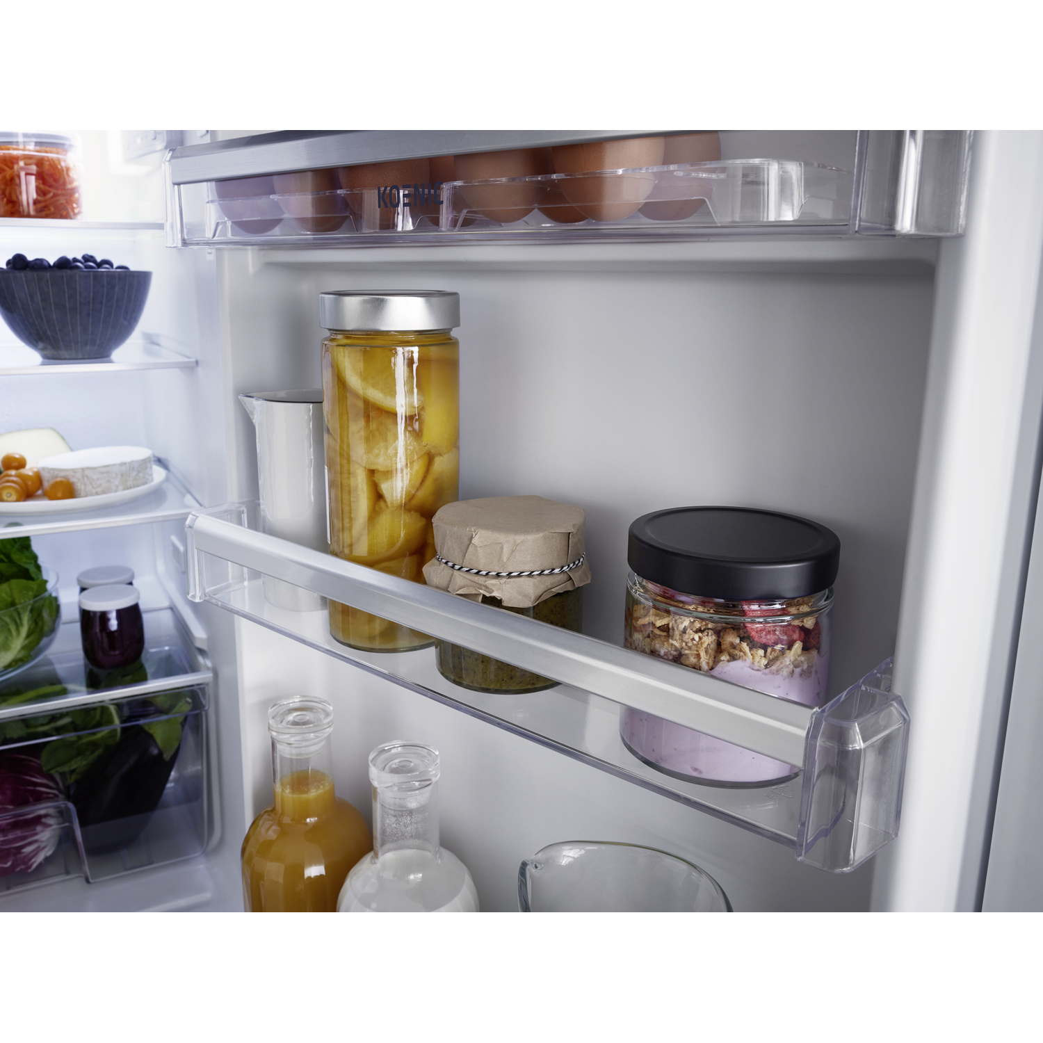 Inside a fridge: eggs, jarred food, juice bottles, cheese, berries, and other items are visible on shelves.