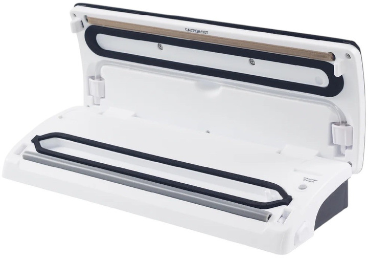 Biała zgrzewarka próżniowa, otwarta pokrywa. Czarne gumowe uszczelki, szary pasek i widoczny tekst 'UWAGA GORĄCE'. Etykieta 'Przełącznik pojemnika'.