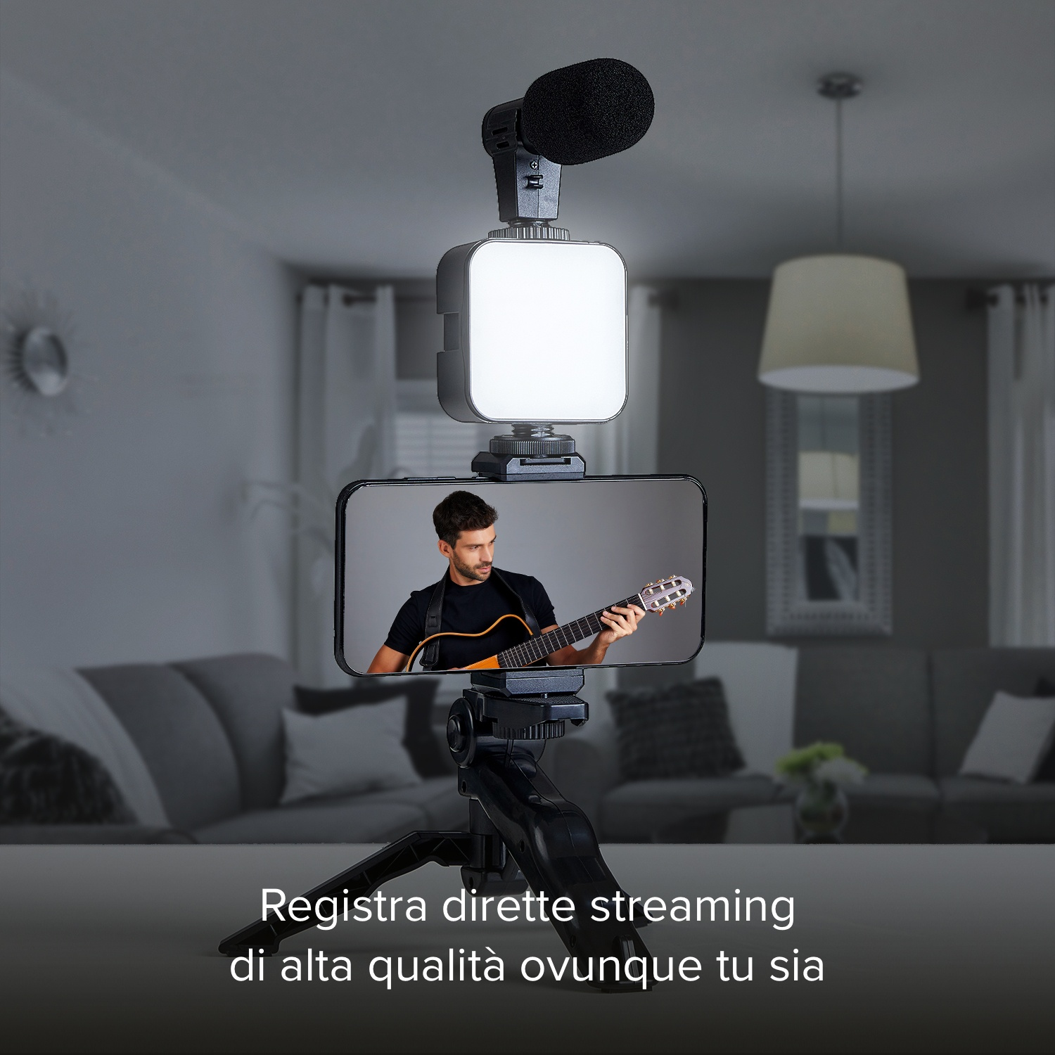 Smartphone con chitarrista sullo schermo, collegato a luce e microfono. Sfondo interno con divano e lampada.