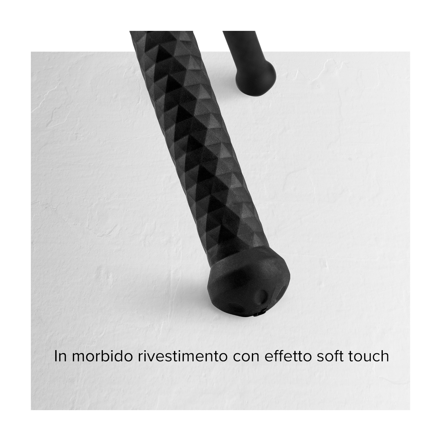 Gamba nera e strutturata di un oggetto su sfondo bianco e strutturato. Un'altra gamba nera è leggermente visibile.