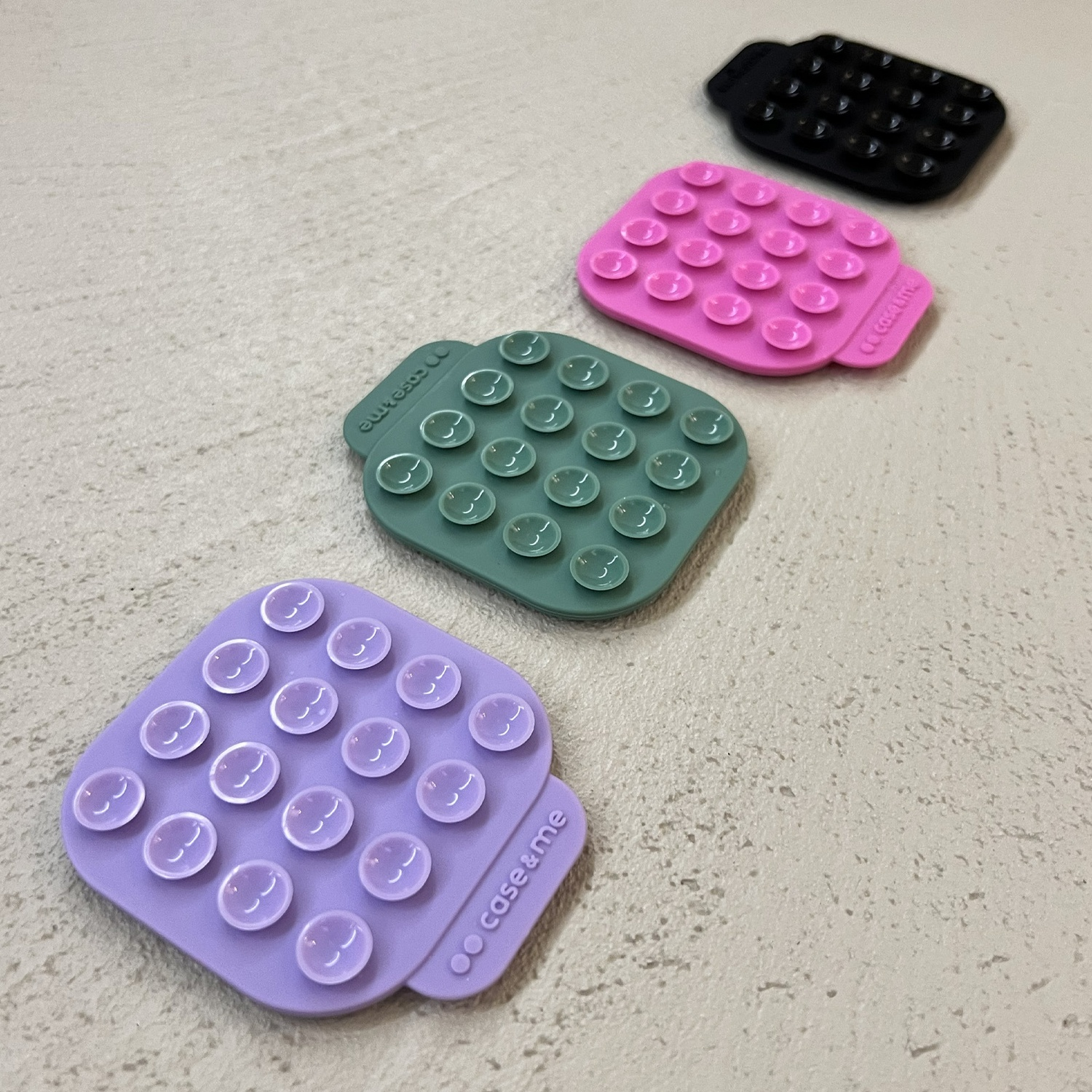 Quattro cuscinetti a ventosa colorati su una superficie strutturata. Colori: viola, verde, rosa e nero. Ogni cuscinetto ha ventose.