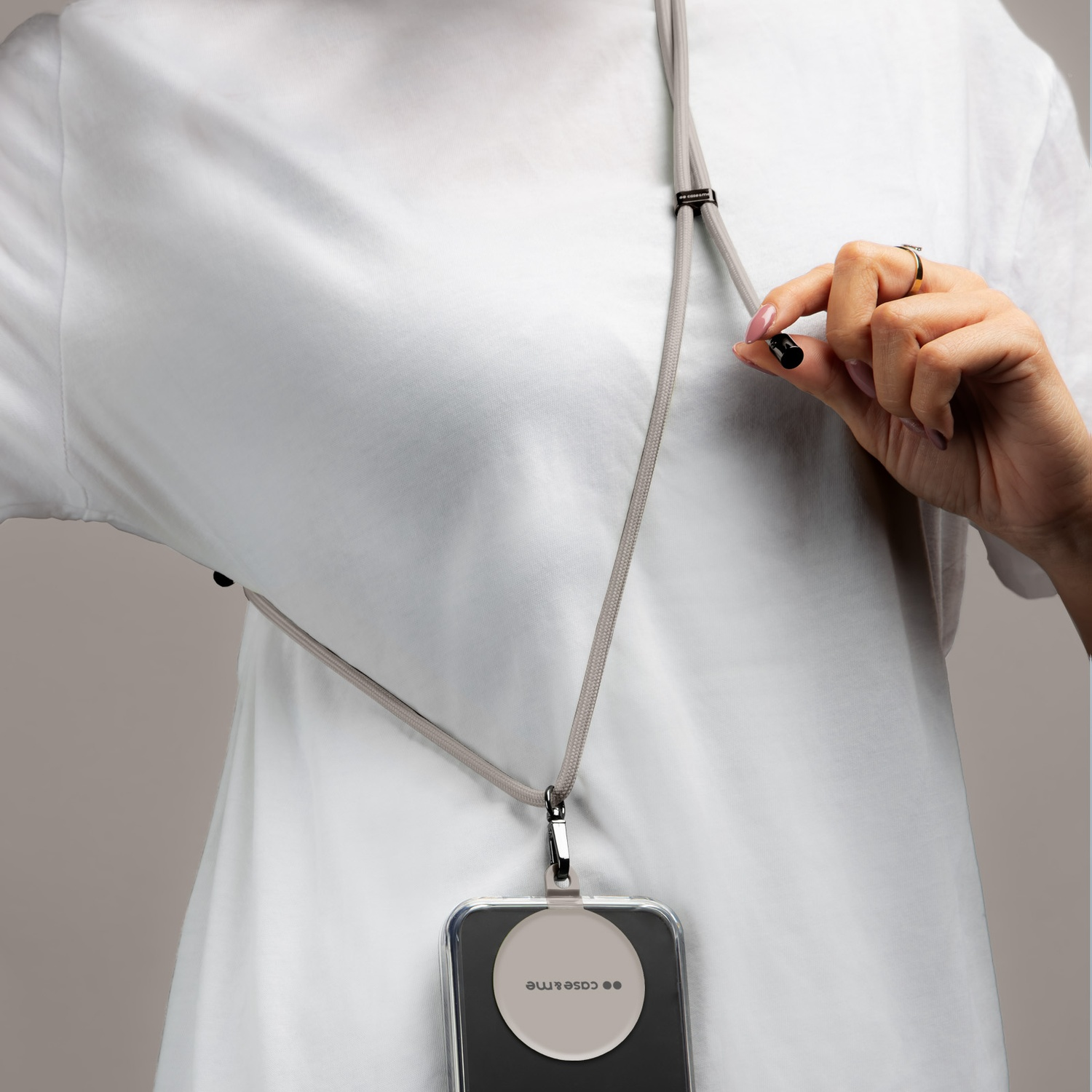 Una persona con una camicia bianca tiene un cordino grigio per telefono. Una custodia trasparente con un cerchio è attaccata.