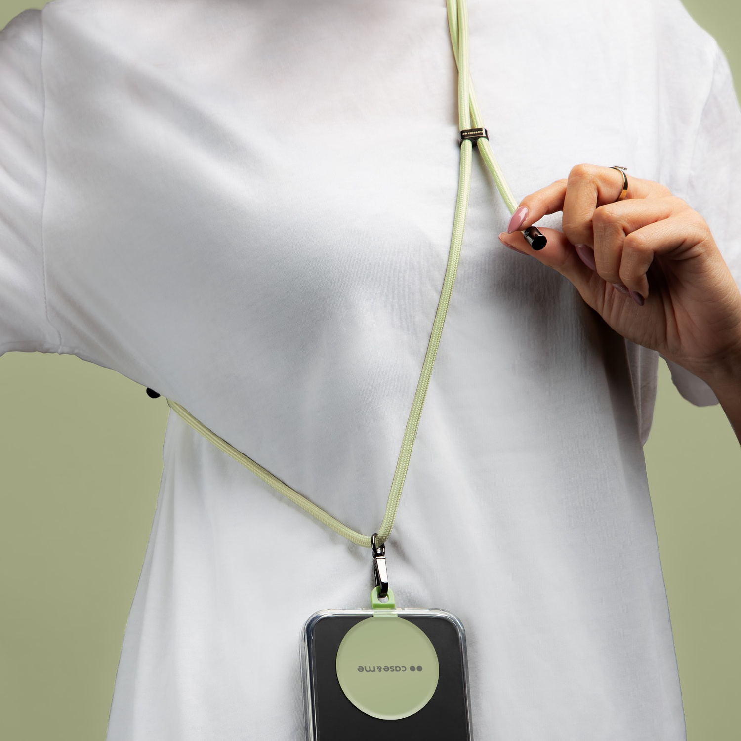 Una persona con una camicia bianca tiene una cinghia per telefono verde chiaro. La custodia del telefono ha un disco verde con il marchio.