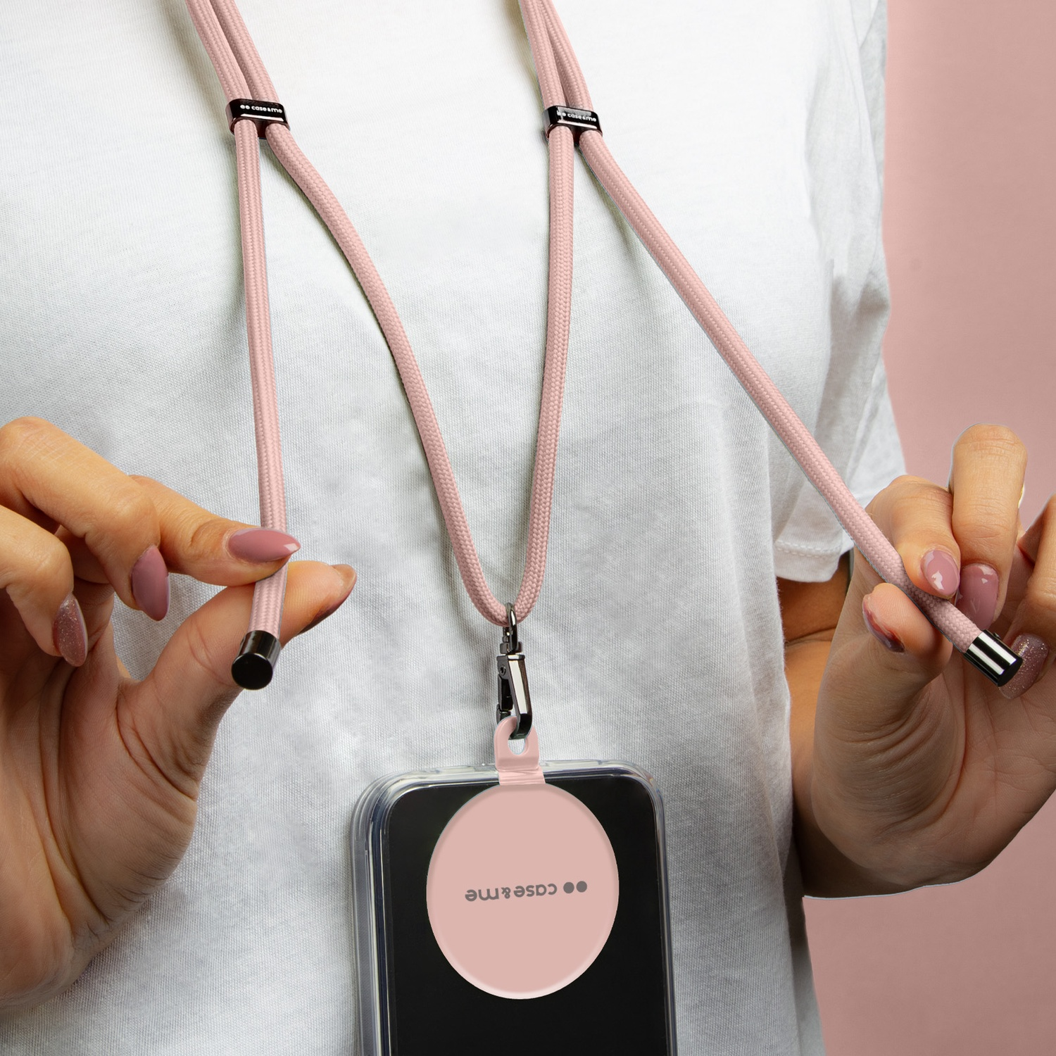 Donna che tiene un cordino rosa per telefono con custodia. Lo sfondo è rosa.