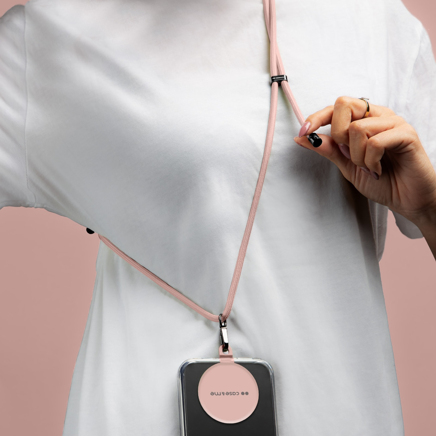Una persona indossa un cinturino rosa per telefono. Una mano tiene un piccolo pezzo nero. Un telefono in una custodia è appeso sotto.