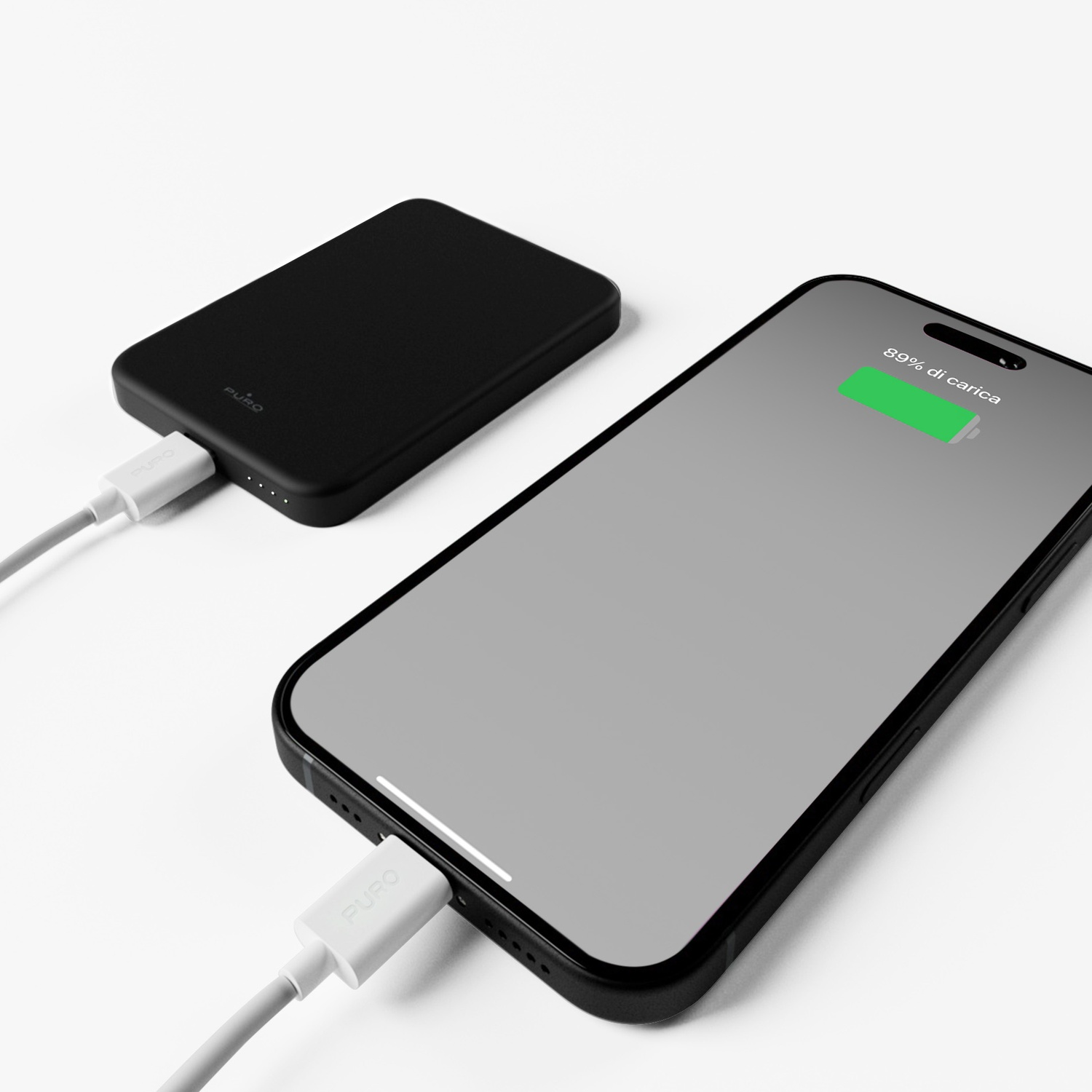 Power bank nera carica un telefono. Il telefono mostra l'89% di carica. Entrambi sono collegati tramite cavi bianchi su superficie bianca.