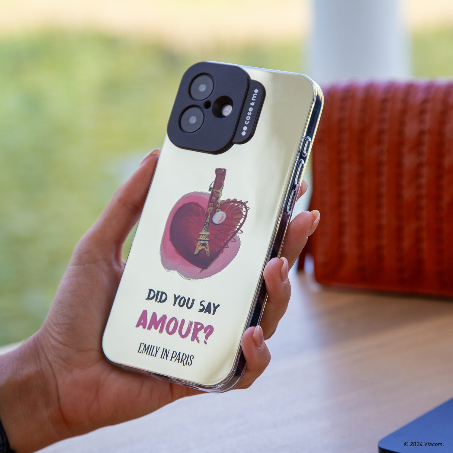 Mano che tiene telefono con design Torre Eiffel e le parole 'Amour?' e 'Emily in Paris'.