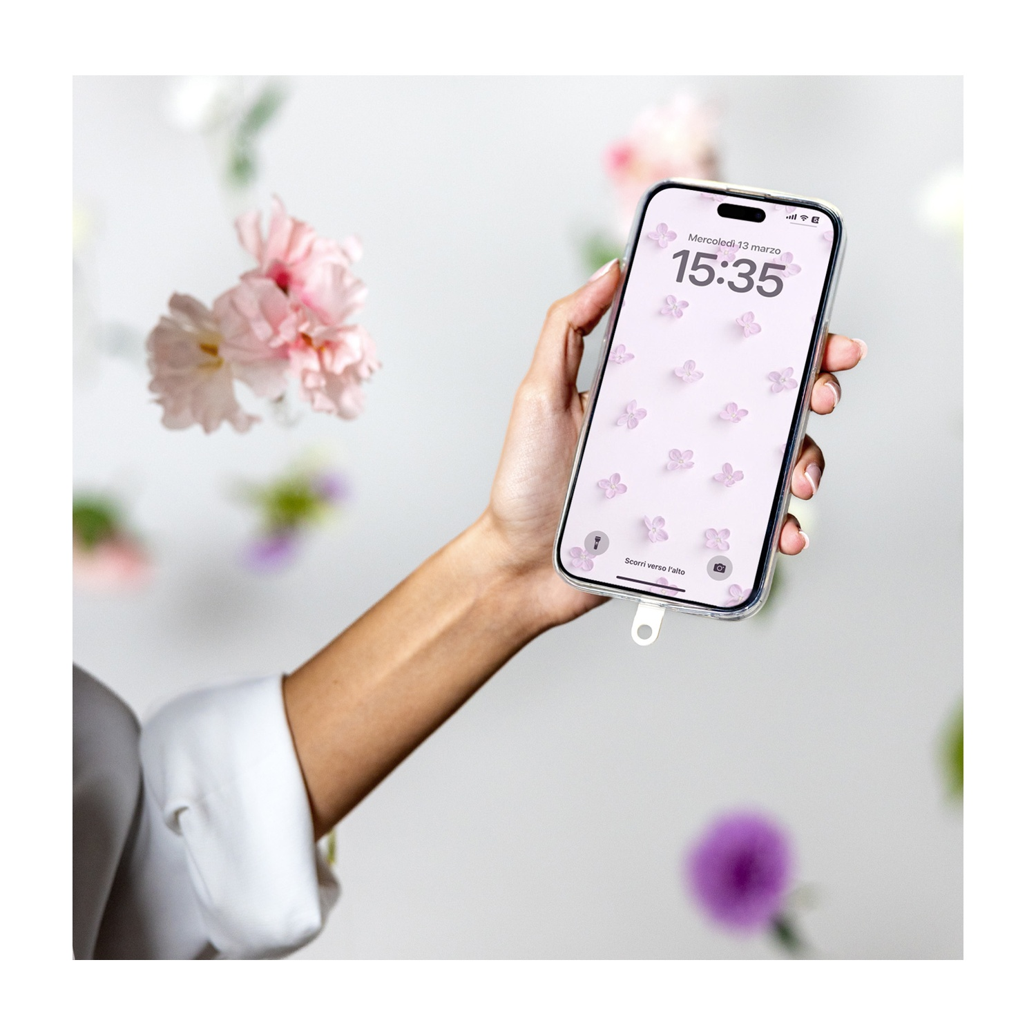 Una mano tiene un telefono con sfondo floreale. Fiori fluttuano intorno. L'ora è 15:35.