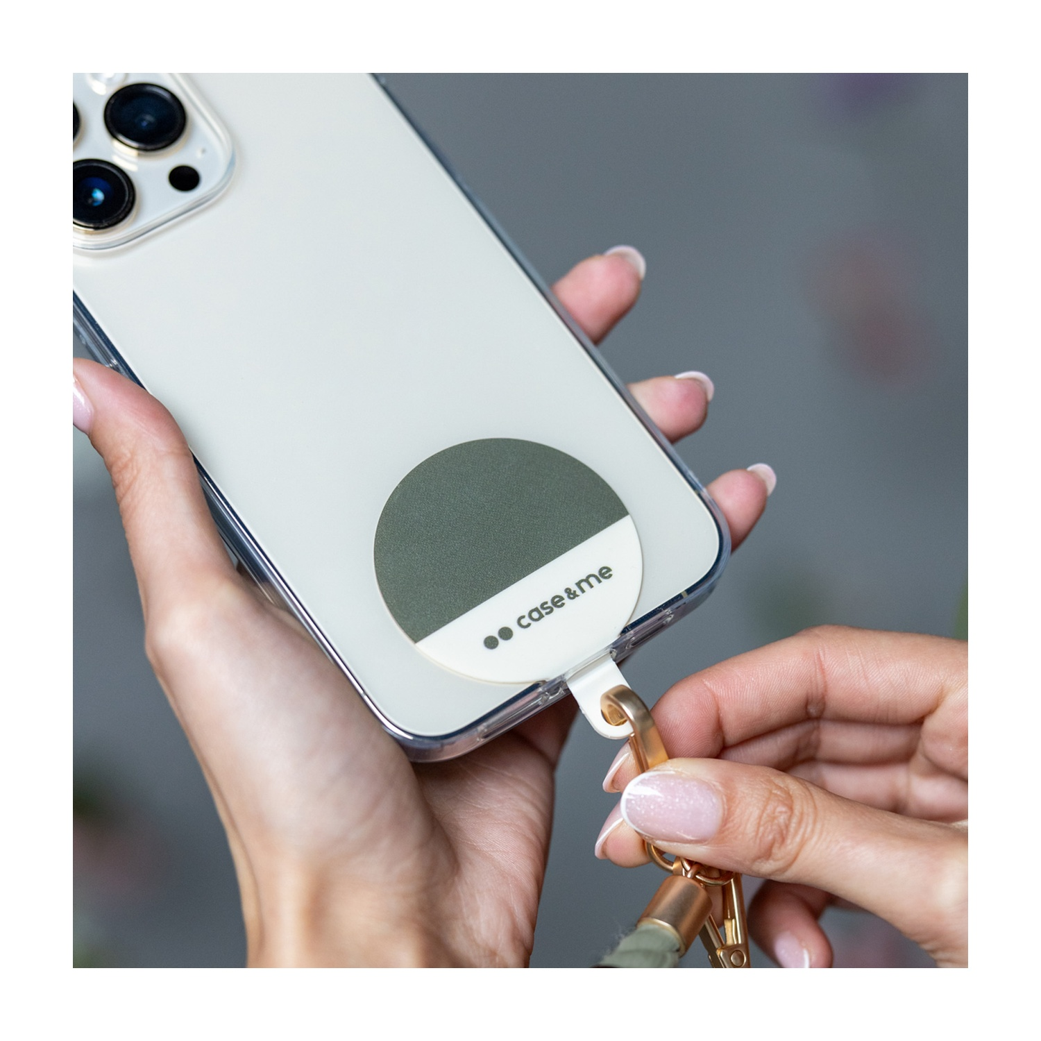 Donna che tiene un telefono con custodia e cinturino. La custodia ha un cerchio verde e logo. Mani visibili, con unghie dipinte.