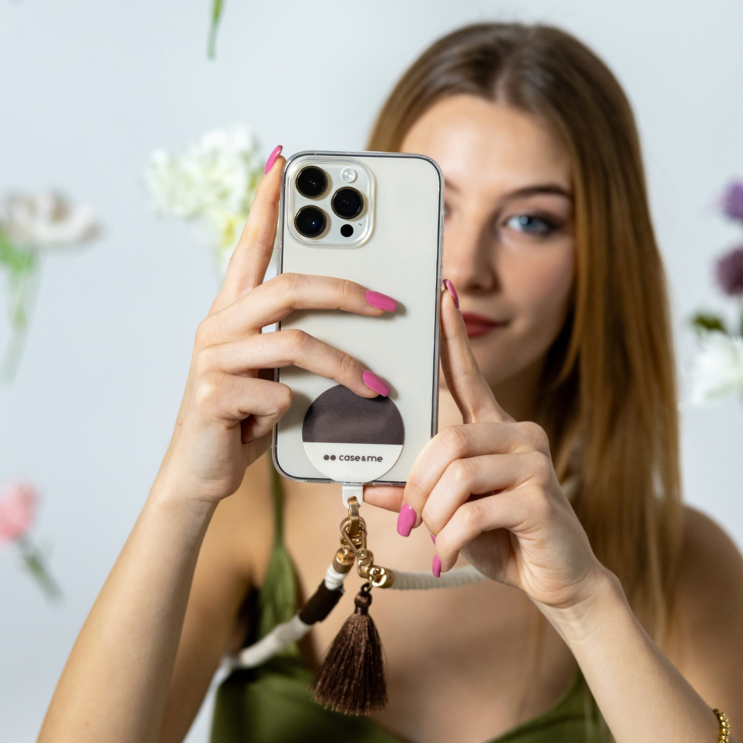 Donna che tiene in mano il telefono. Il telefono ha una custodia con supporto e cinturino. Fiori sullo sfondo sfocati.