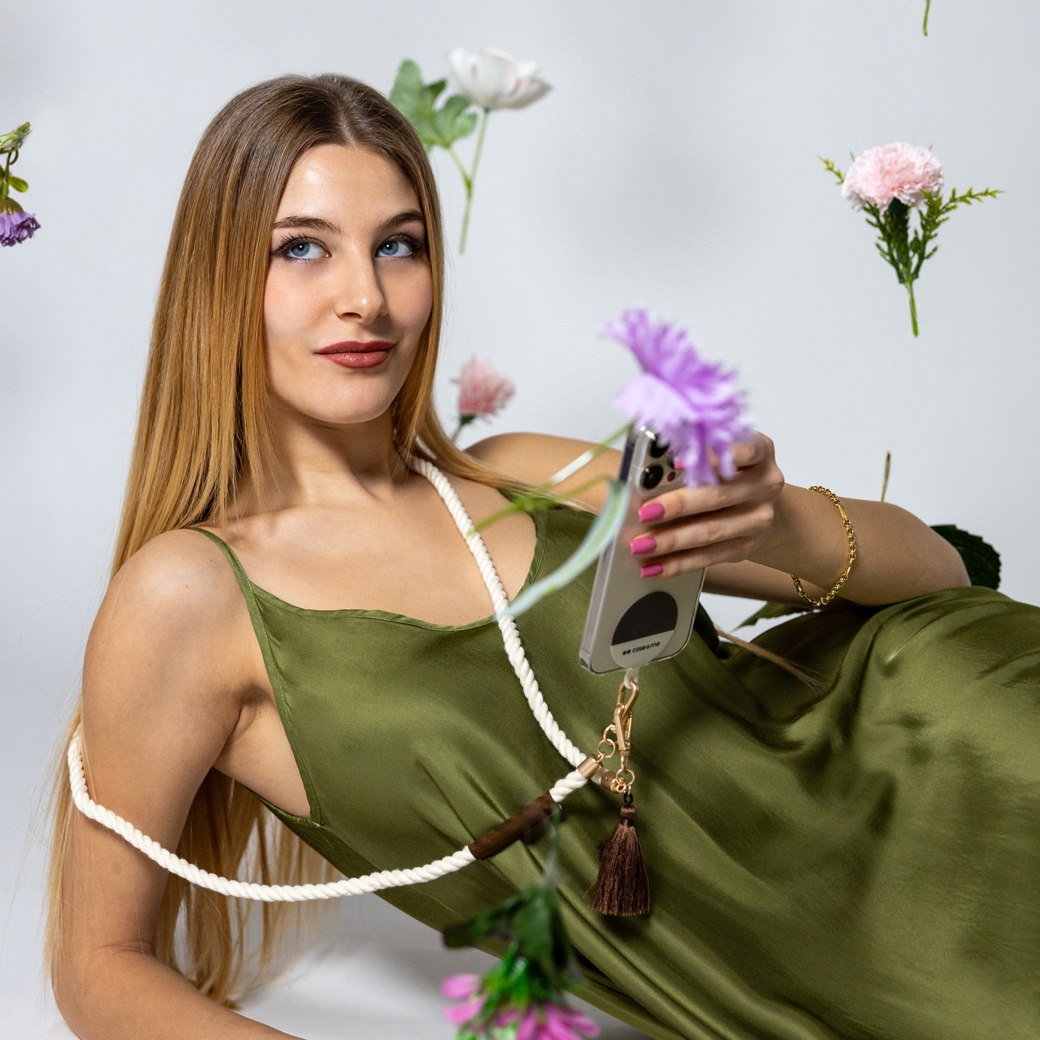 Donna in abito verde che tiene in mano un telefono con cordino, fiori intorno. Guarda in su. Sfondo bianco.