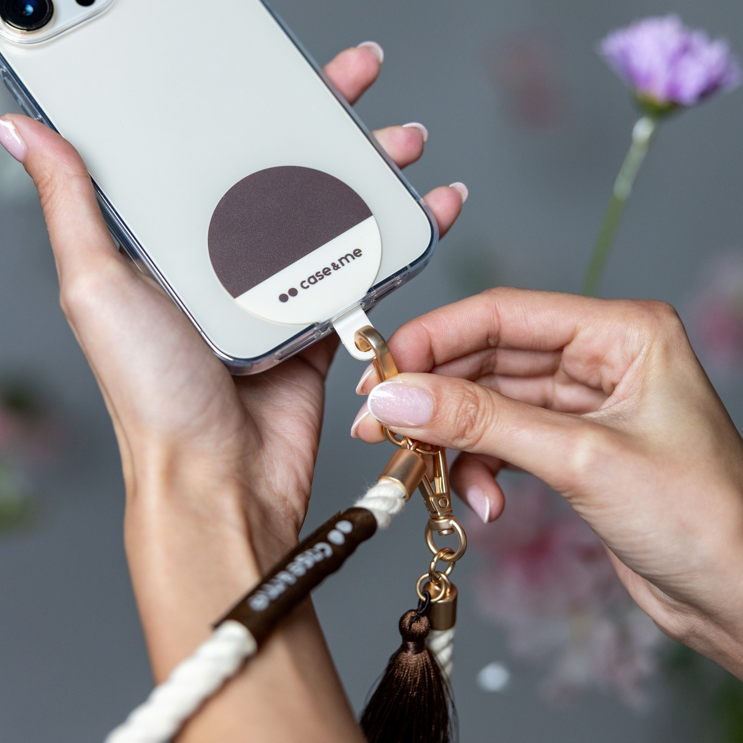 Mani che collegano un cinturino del telefono a una custodia. Il cinturino è bianco e marrone. Il telefono è bianco.