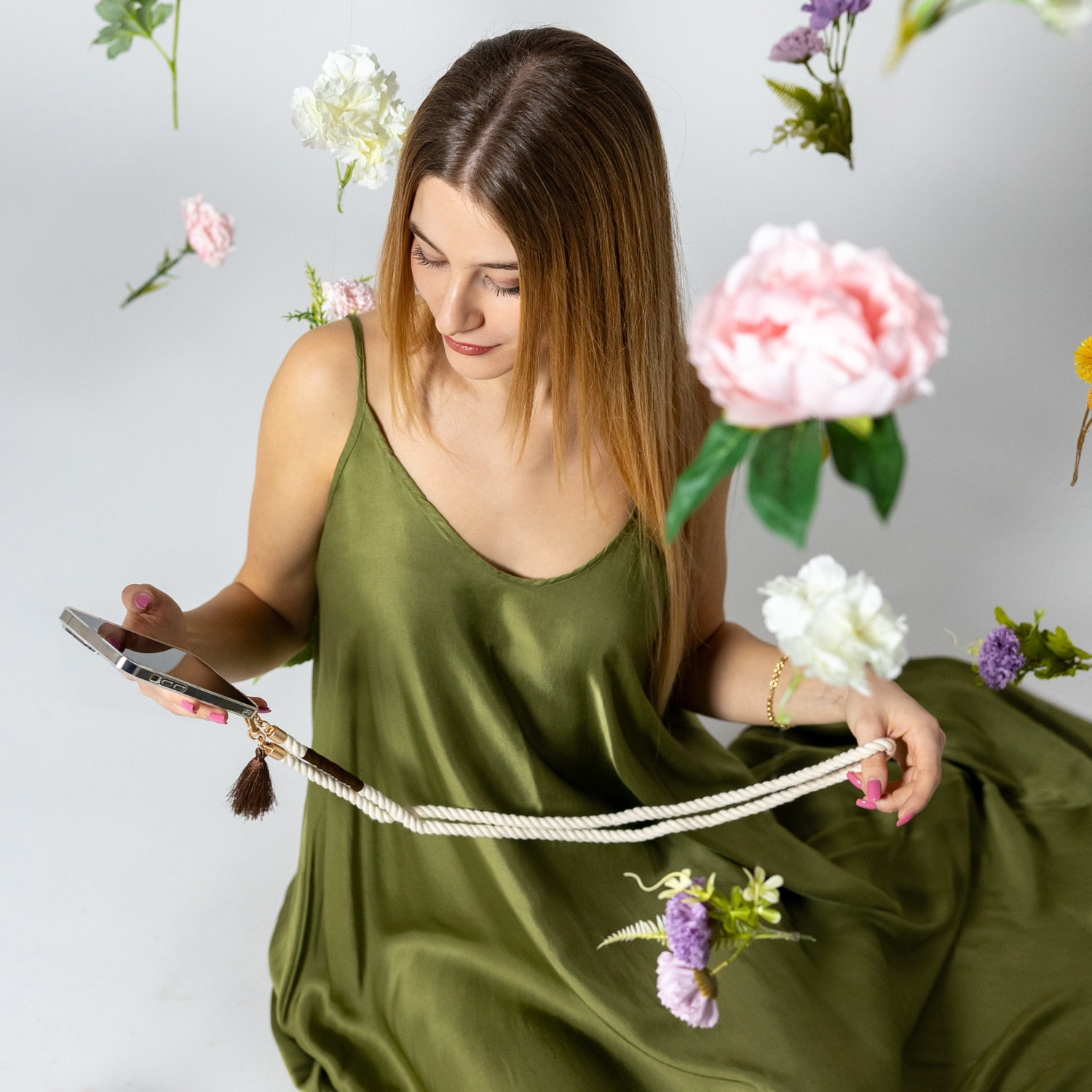 Donna in abito verde tiene telefono con corda. Fiori fluttuanti. Sfondo bianco.