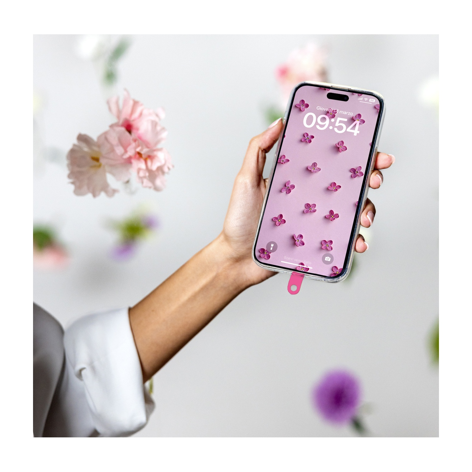 Una mano tiene un telefono con sfondo floreale. Fiori rosa circondano il telefono. Lo sfondo è bianco con fiori.