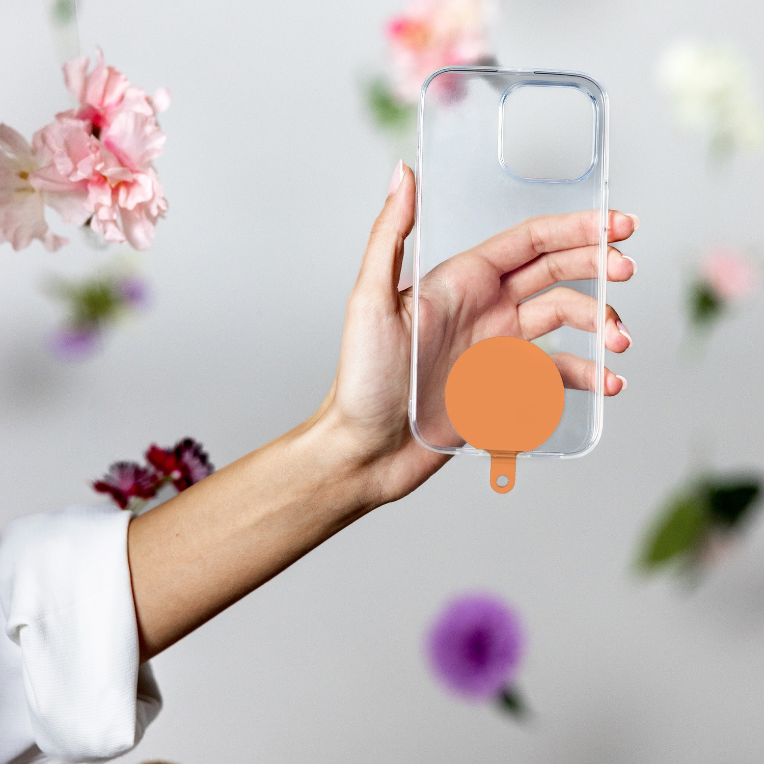 Mano che tiene una custodia trasparente per telefono con cerchio arancione. Fiori sullo sfondo.
