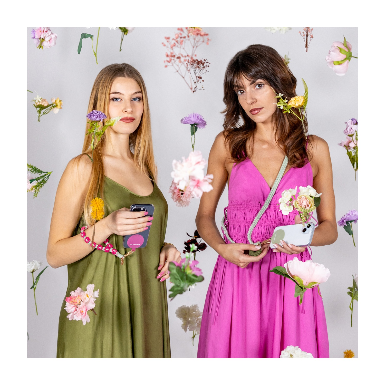 Due donne con telefoni, accessori floreali e abiti, circondate da fiori su sfondo bianco.