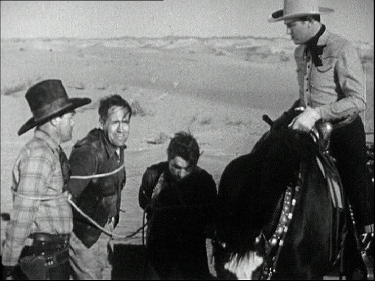 Cowboy auf Pferd mit 3 gefesselten Männern. Wüstenhintergrund. Schwarzweißfoto.