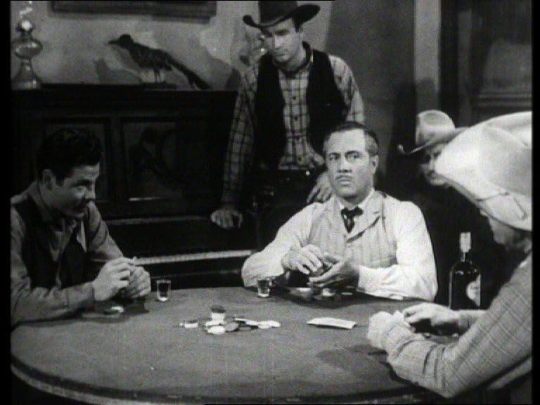 Männer spielen Poker in einem Saloon. Ein Gemälde eines Vogels hängt am Klavier. Whiskeyflasche auf dem Tisch.