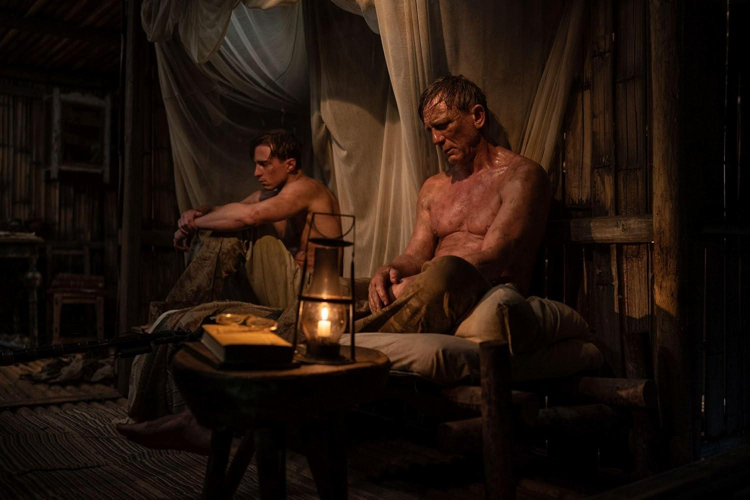 Zwei Männer sitzen in einem dunklen Raum mit einer brennenden Lampe.