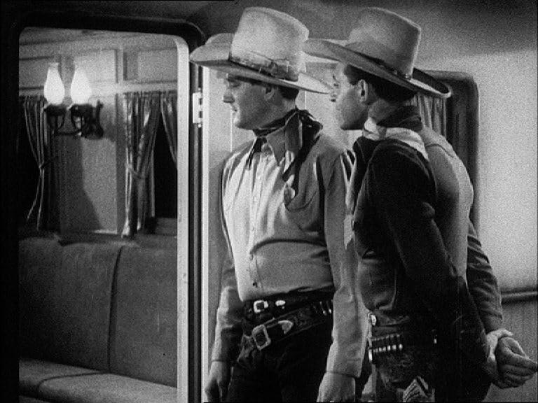 Zwei Männer mit Cowboyhüten stehen an einer Bahntür. Einer trägt ein Sheriff-Abzeichen. Im Inneren befinden sich eine Couch und Lampen.