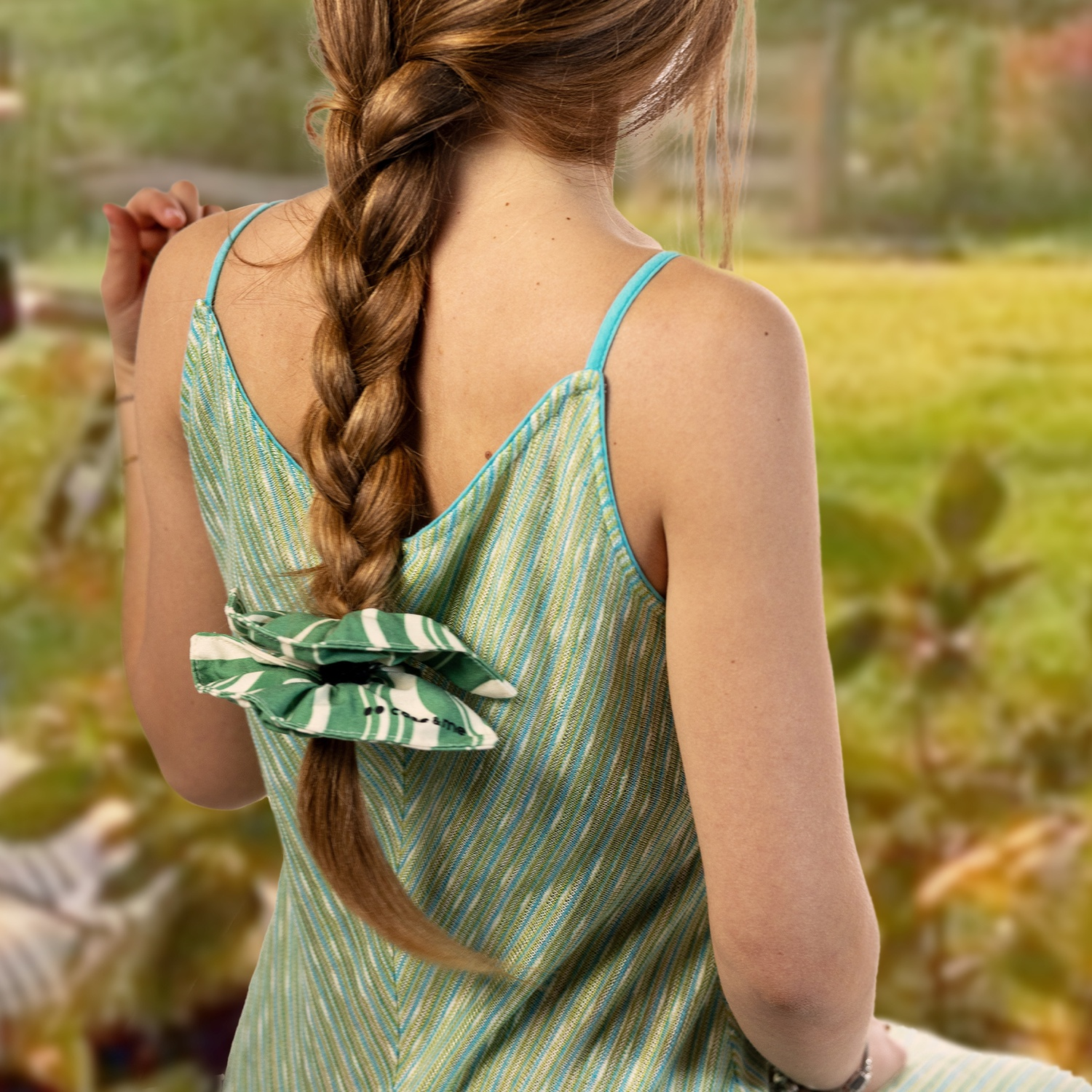 Una donna con lunghi capelli castano intrecciati. Indossa un vestito a righe verdi e blu. I capelli sono legati con un elastico verde a fantasia.