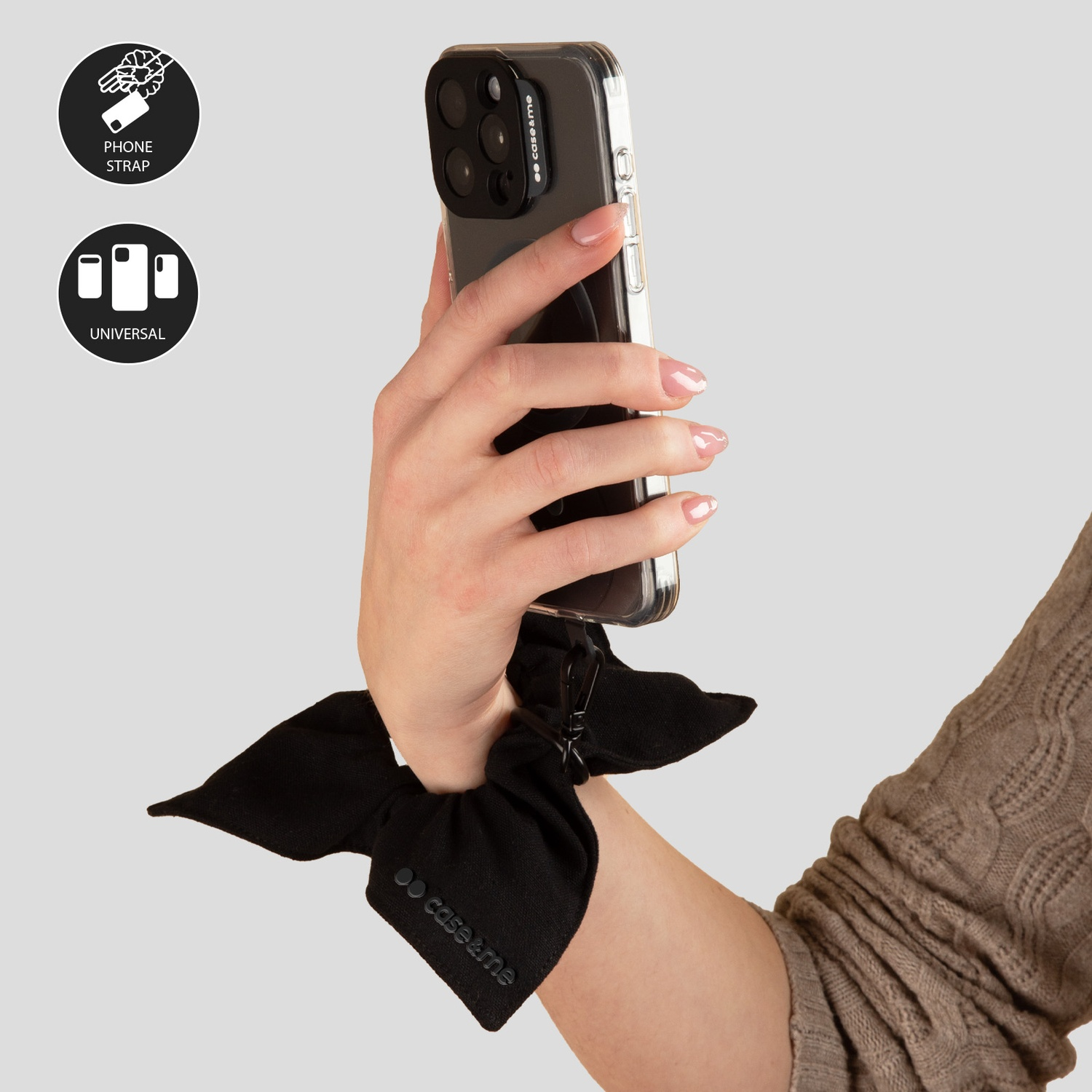 Mano che tiene il telefono in una custodia trasparente con uno scrunchie nero. Icone per cinturino telefono e uso universale a sinistra.