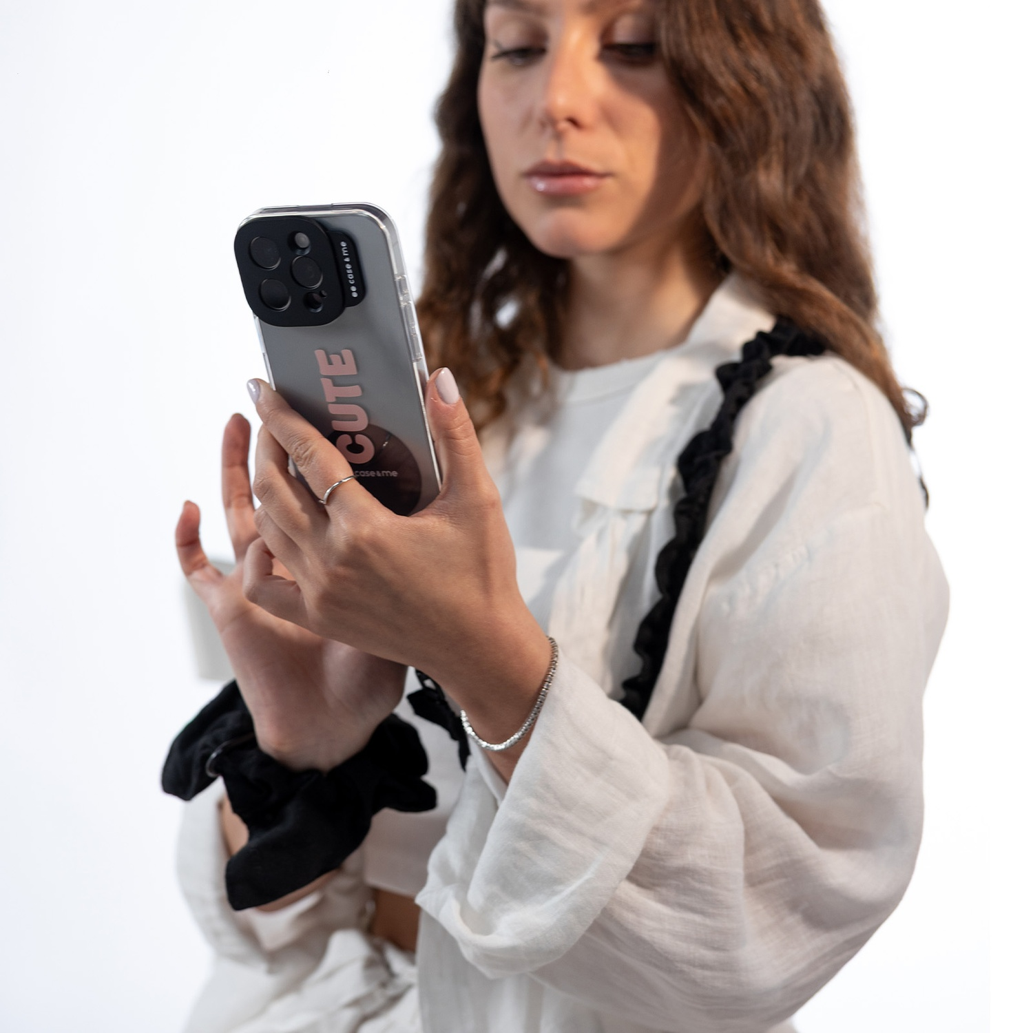 Donna che tiene in mano un telefono con una custodia rosa 'cute'. Indossa una camicia bianca con finiture nere, anello e bracciale d'argento.