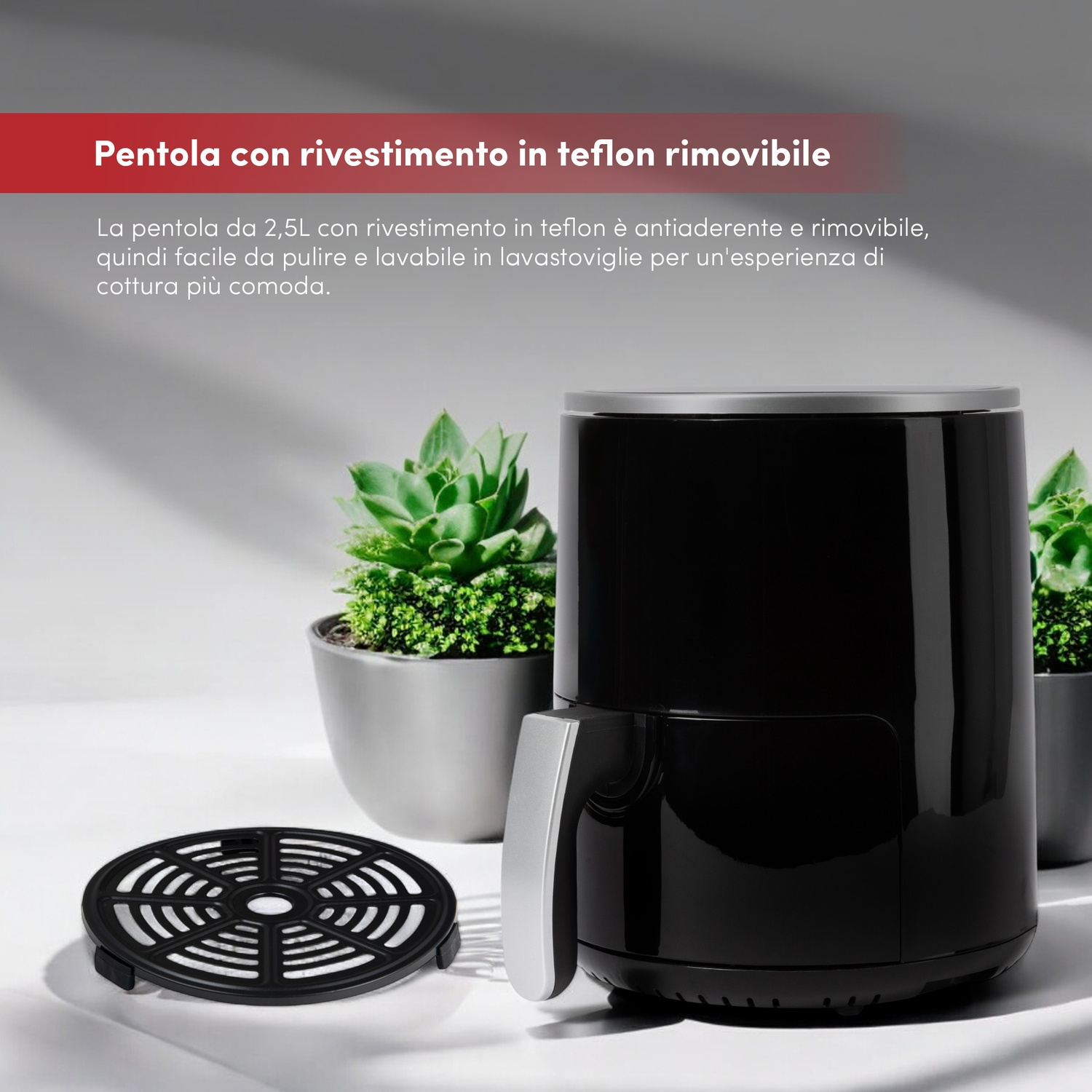 Friggitrice ad aria nera con manico argentato e griglia nera. Due piante in vaso dietro.