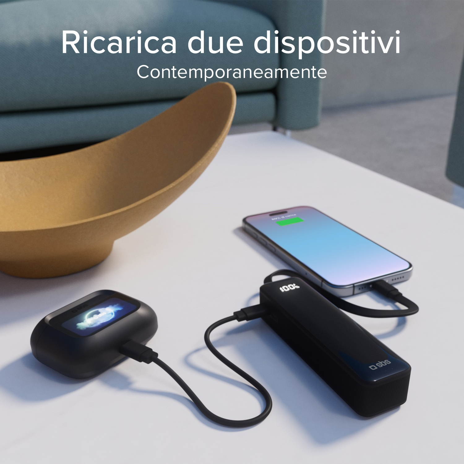 Un telefono e un power bank nero si stanno caricando su un tavolo bianco. Anche un altro dispositivo è in carica. Una ciotola dorata è sul tavolo.