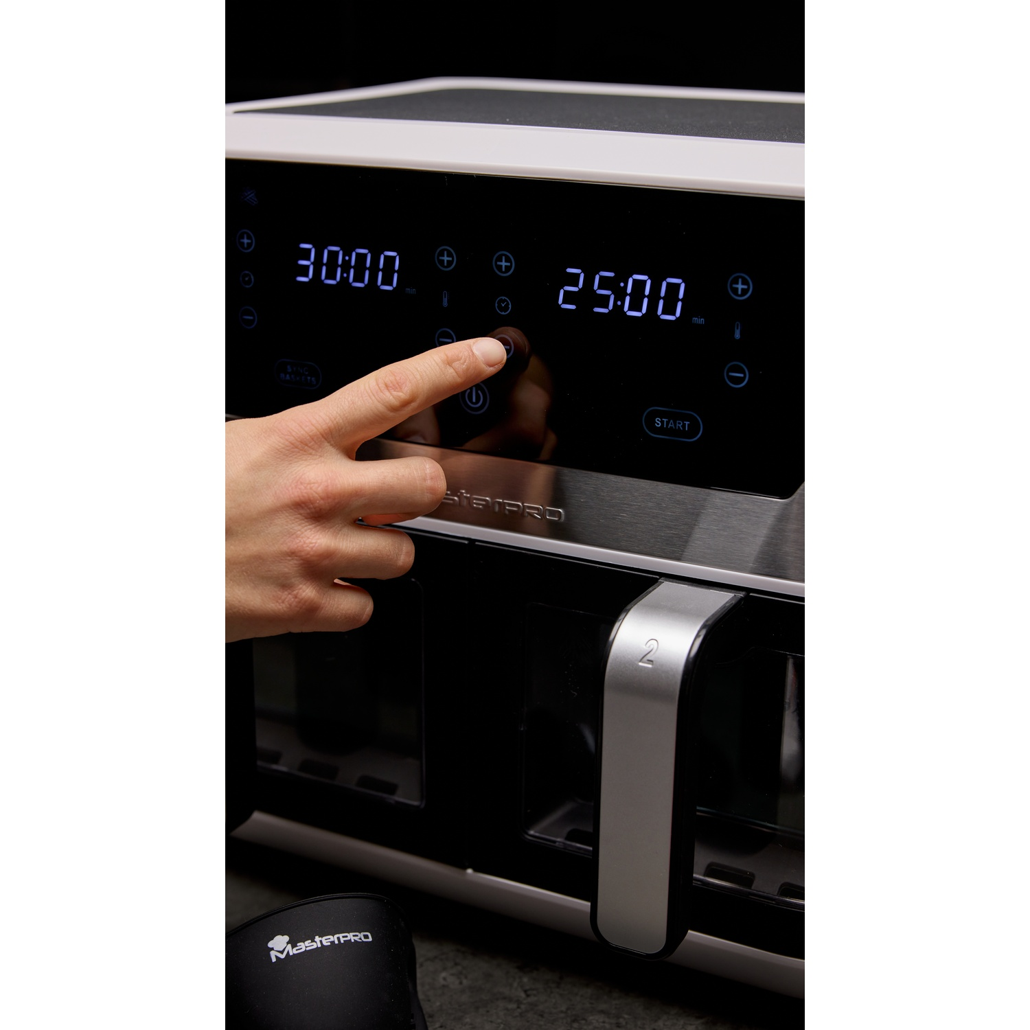Una mano preme il pulsante di accensione di una friggitrice ad aria. Il display mostra 30:00 e 25:00. Il dispositivo è nero e argento.