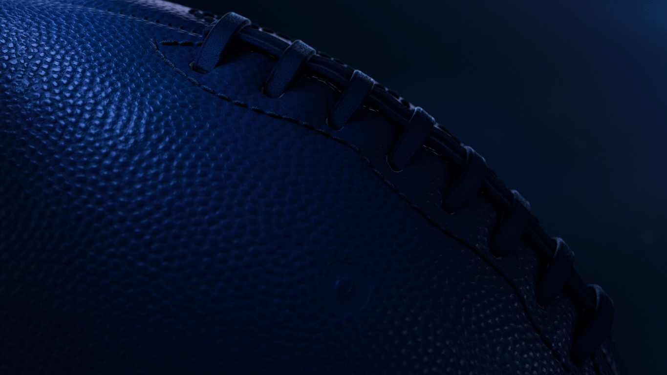 Zbliżenie niebieskiej piłki do futbolu amerykańskiego. Widoczne szwy, sznurowanie i faktura. Ciemnoniebieskie tło.
