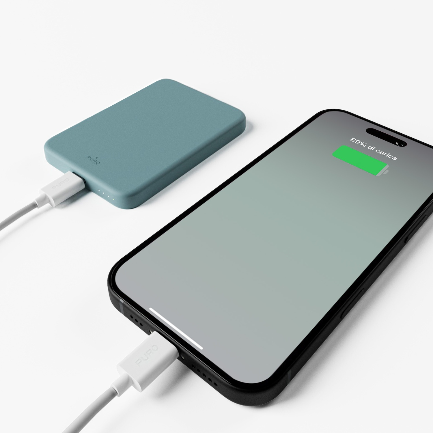 Telefono in carica da un power bank verde acqua. Il telefono mostra l'89% di carica. Entrambi collegati tramite cavi bianchi.