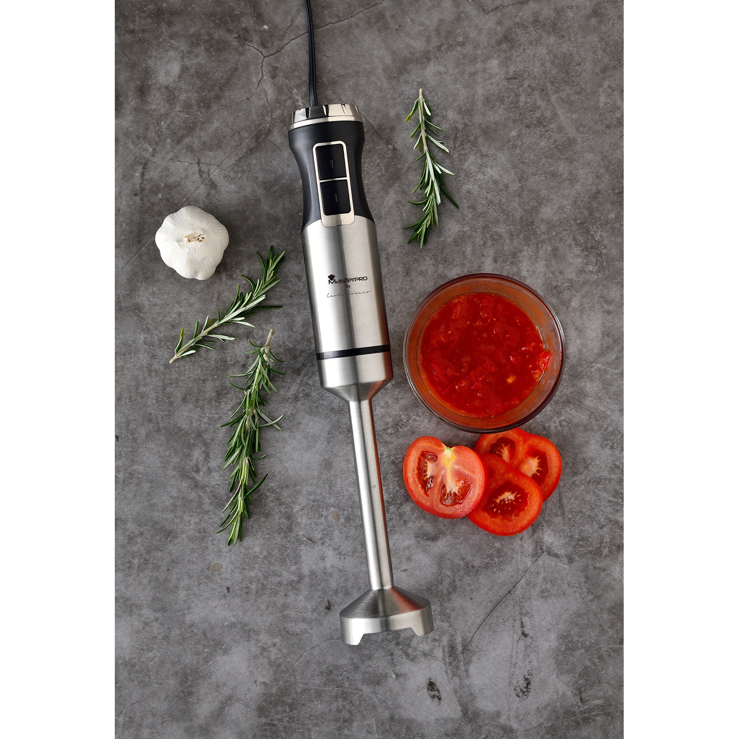 Vista dall'alto: frullatore, pomodori, salsa, aglio e rosmarino su superficie grigia.