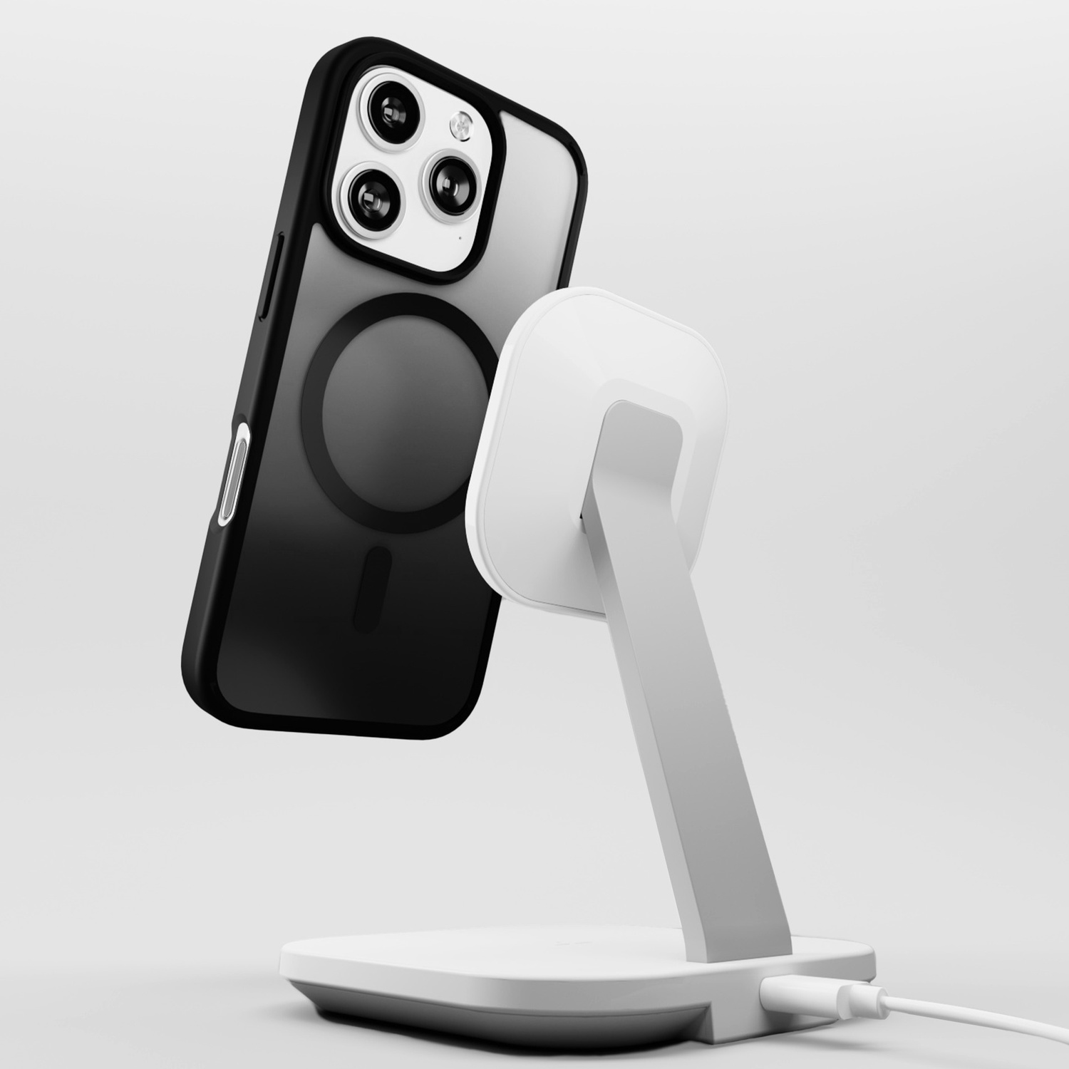 iPhone nero in una custodia sospeso sopra un supporto di ricarica bianco. Il supporto è collegato a un cavo. Sfondo bianco.