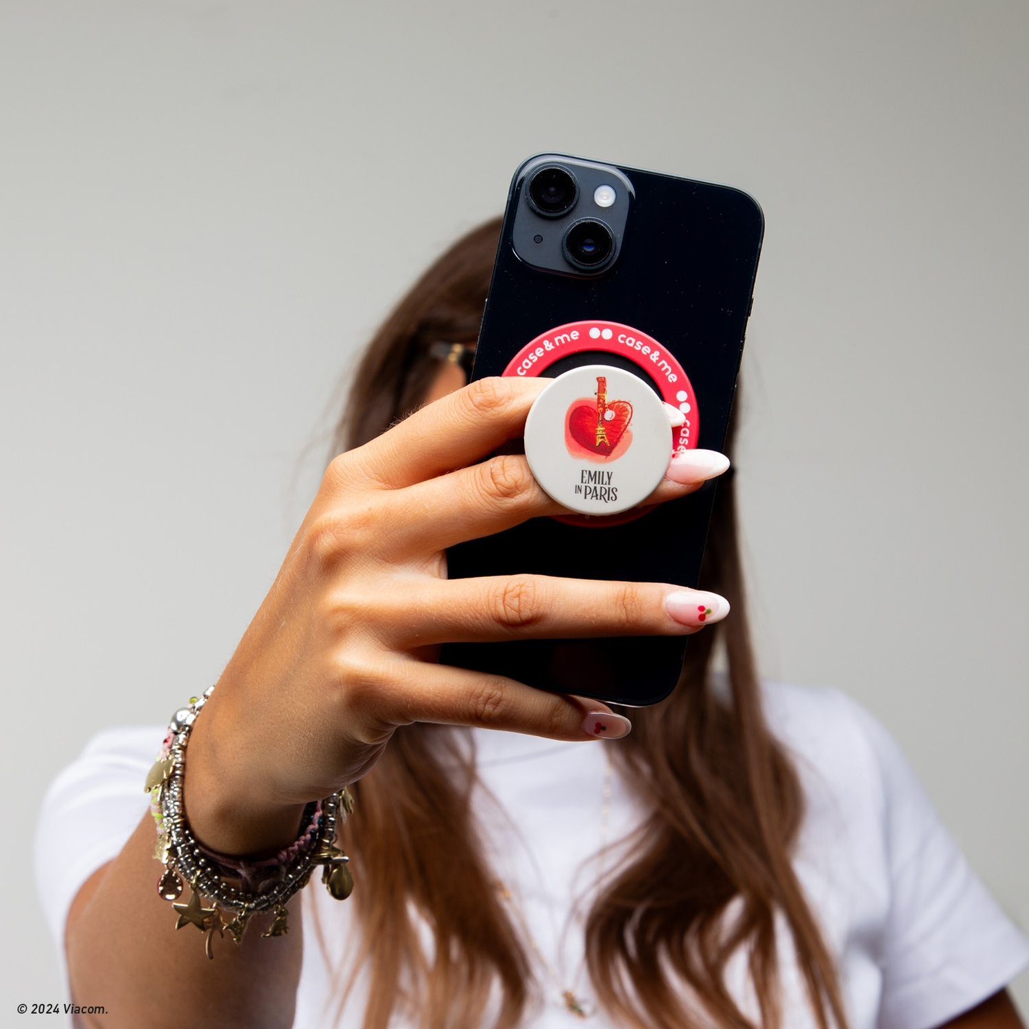 Una donna tiene in mano un telefono nero con un popsocket con un design della Torre Eiffel, che si fa un selfie.