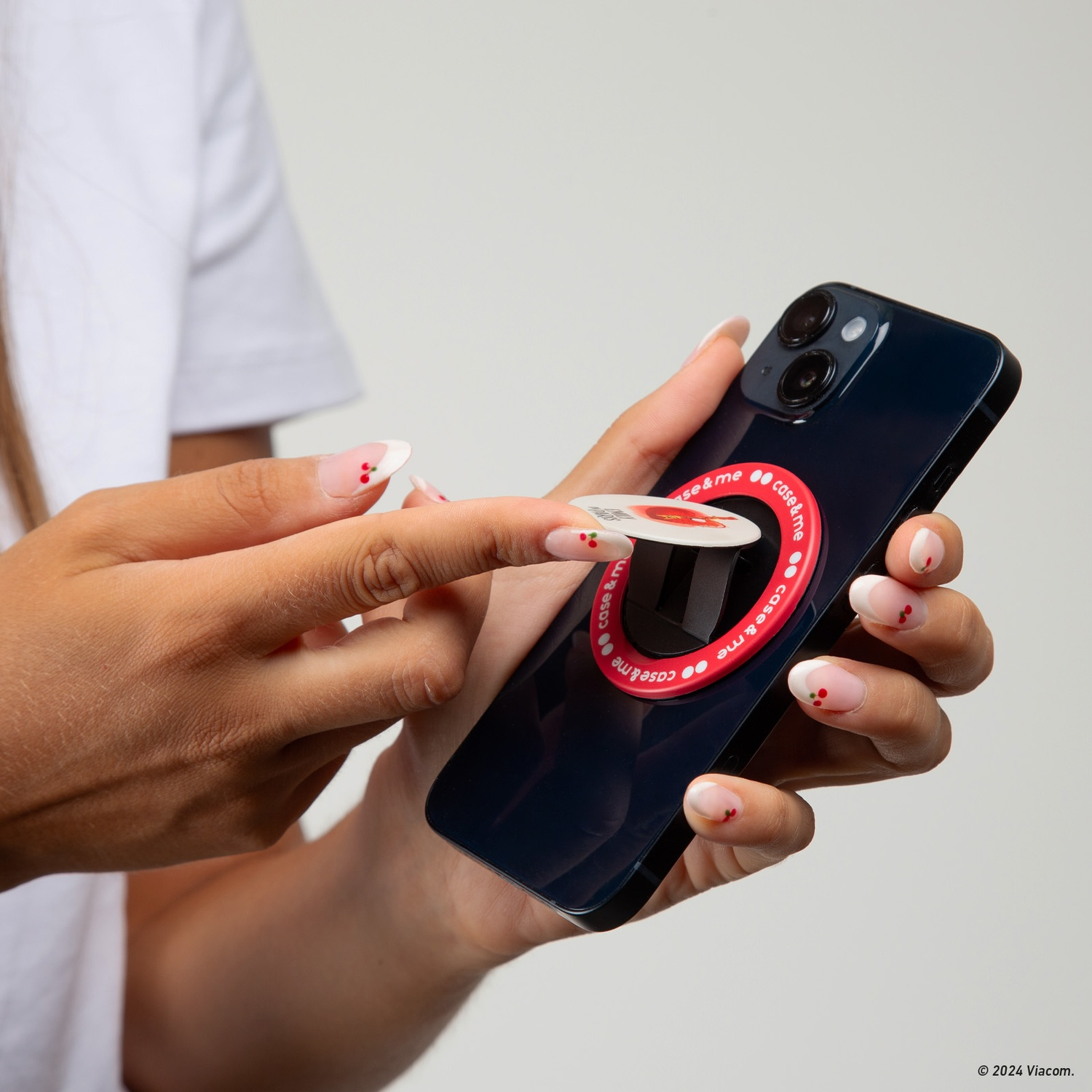 Una persona tiene in mano un telefono con un'impugnatura rossa e bianca. Il telefono è blu scuro. La persona ha le unghie curate.