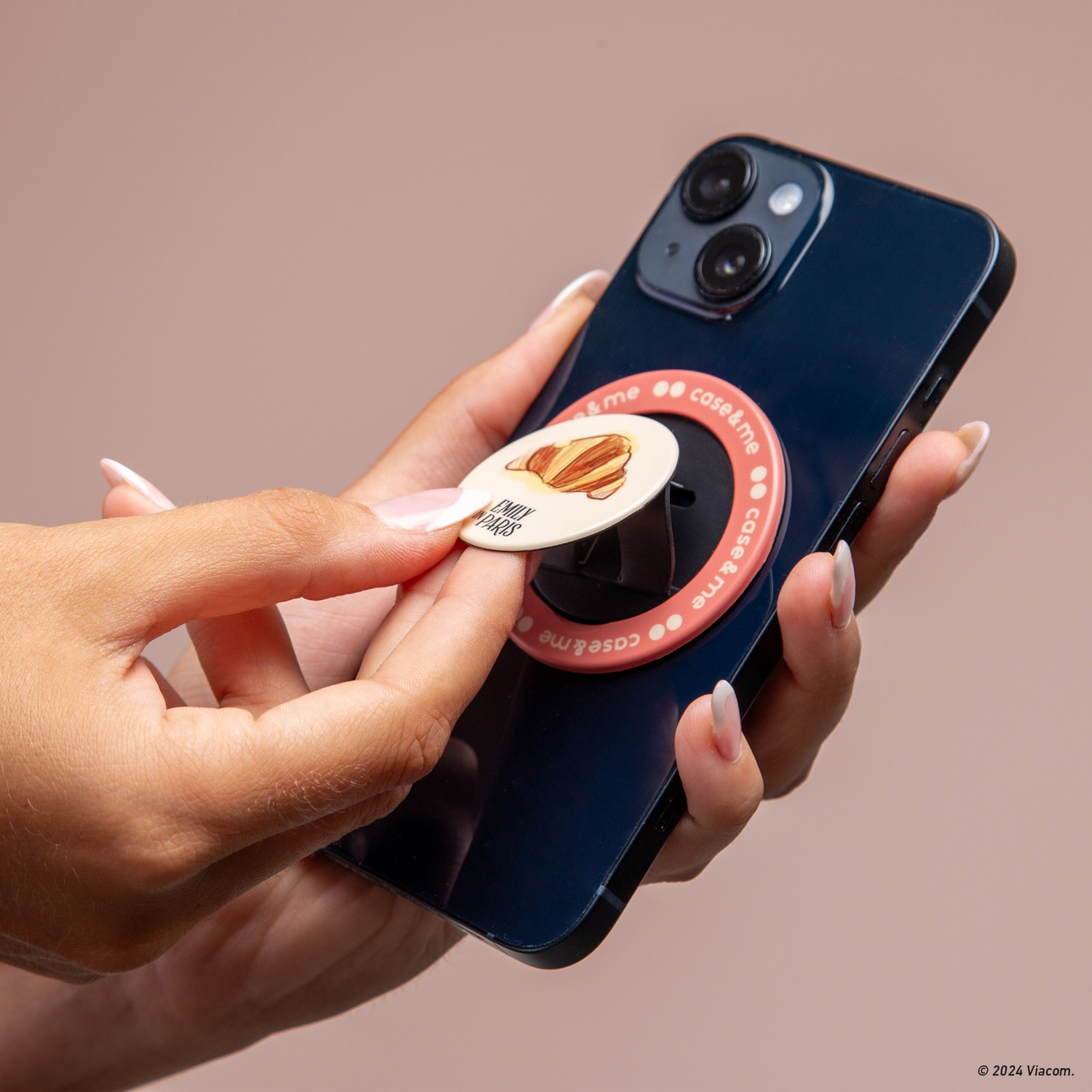 Mano che tiene un telefono con un'impugnatura pop-up con un design a croissant. Il telefono è blu navy con impugnatura rosa.