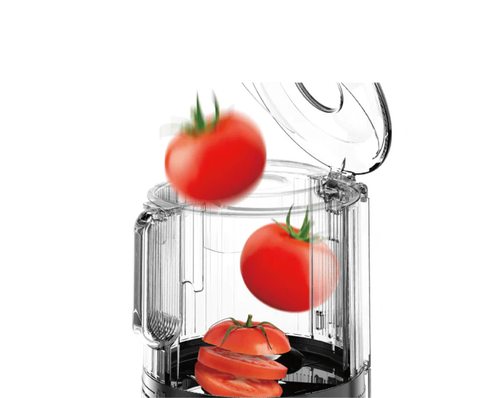 Tomaten fallen in einen transparenten Food Processor. Geschnittene Tomaten liegen unten.