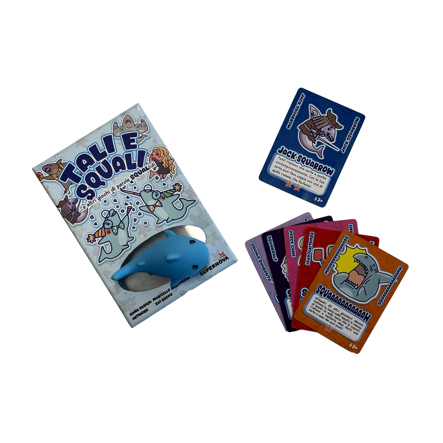 Su una superficie bianca, una scatola di gioco, un giocattolo antistress a forma di squalo e carte. Le carte mostrano illustrazioni di squali e testo.